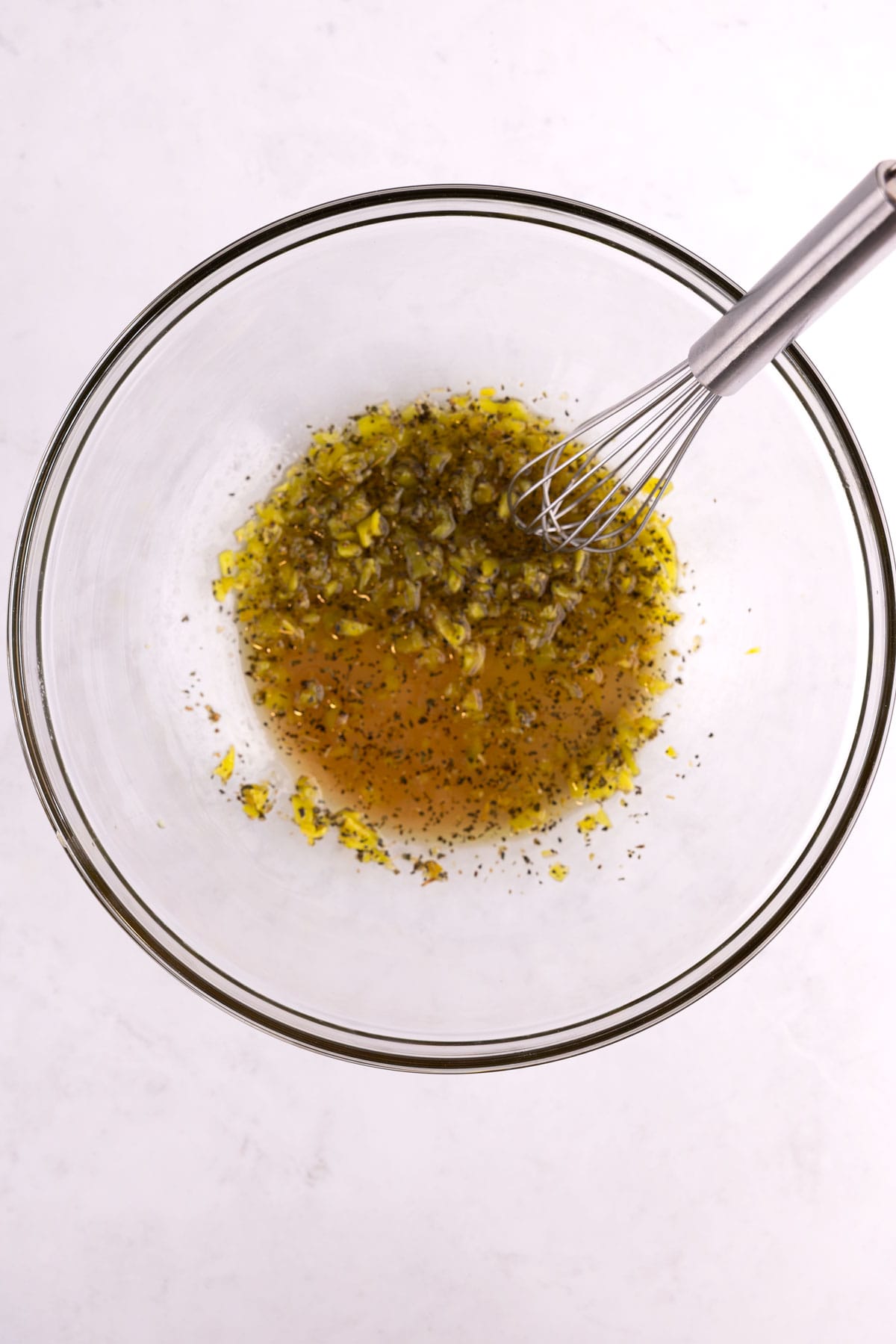 A glass mixing bowl of dressing with a whisk.