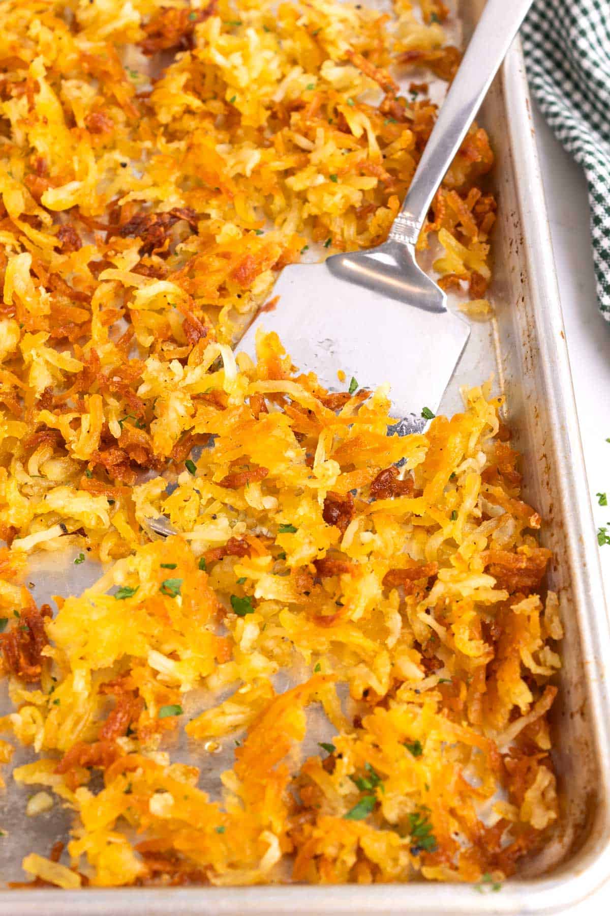 A metal spatula scooping hash browns off of a sheet pan.