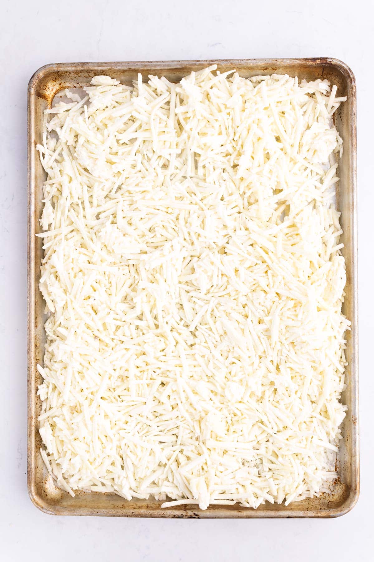 Frozen potato shreds spread out on a cooking pan.