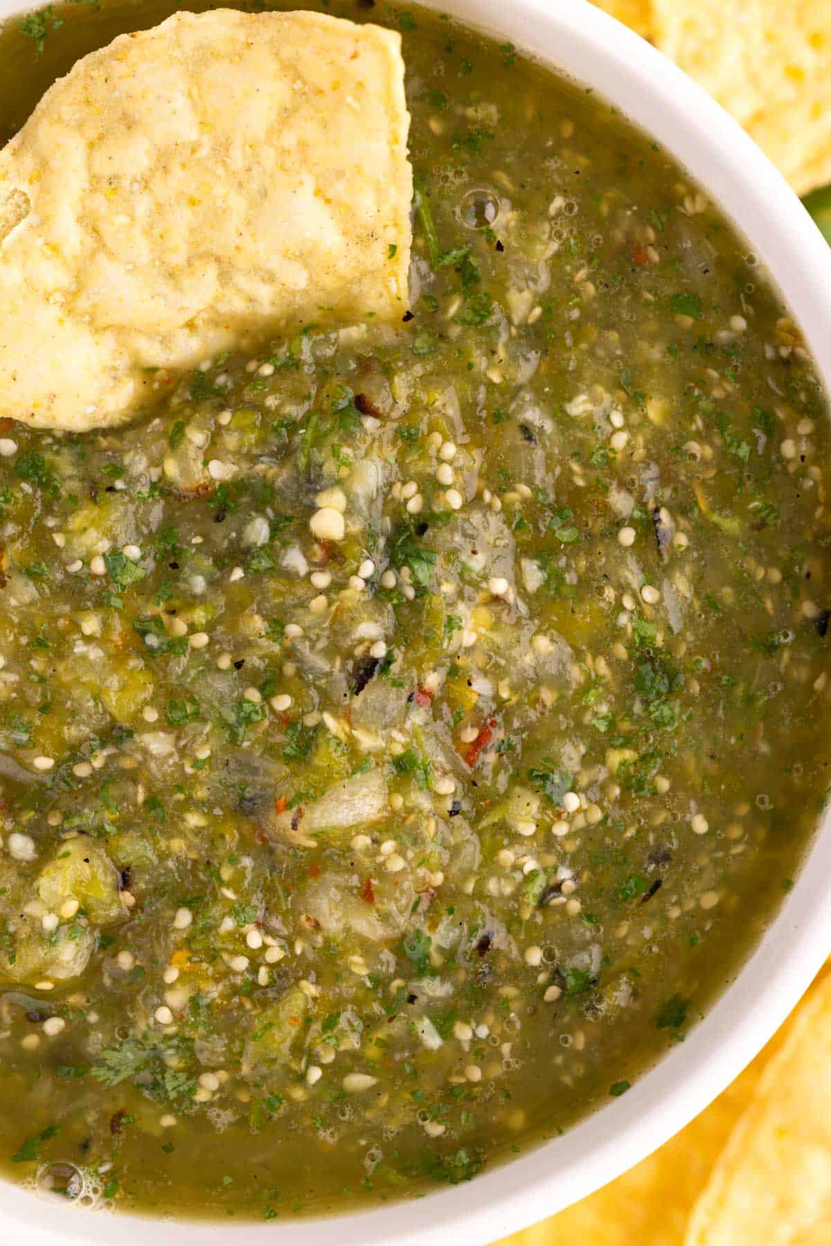 A bowl of green salsa with a chip dipped into it.