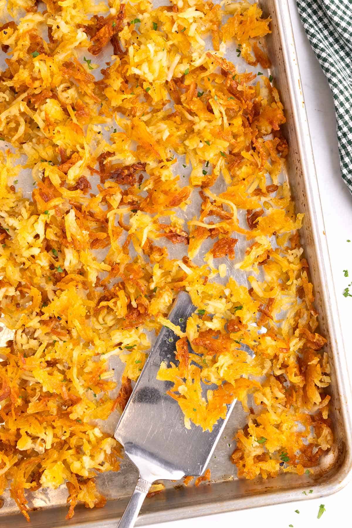 A cookie sheet full of hash browns with a serving spatula.
