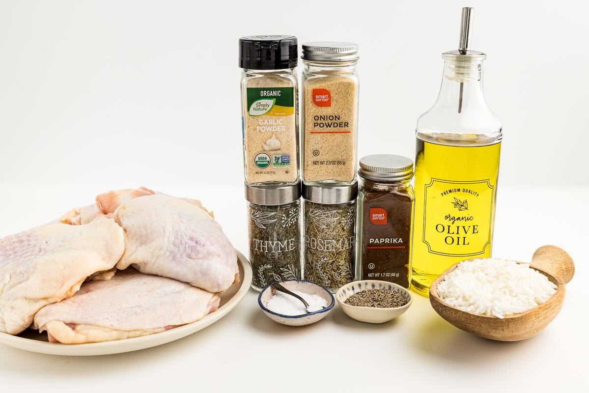 Chicken thighs, salt, seasonings, rice, and olive oil on a white surface.