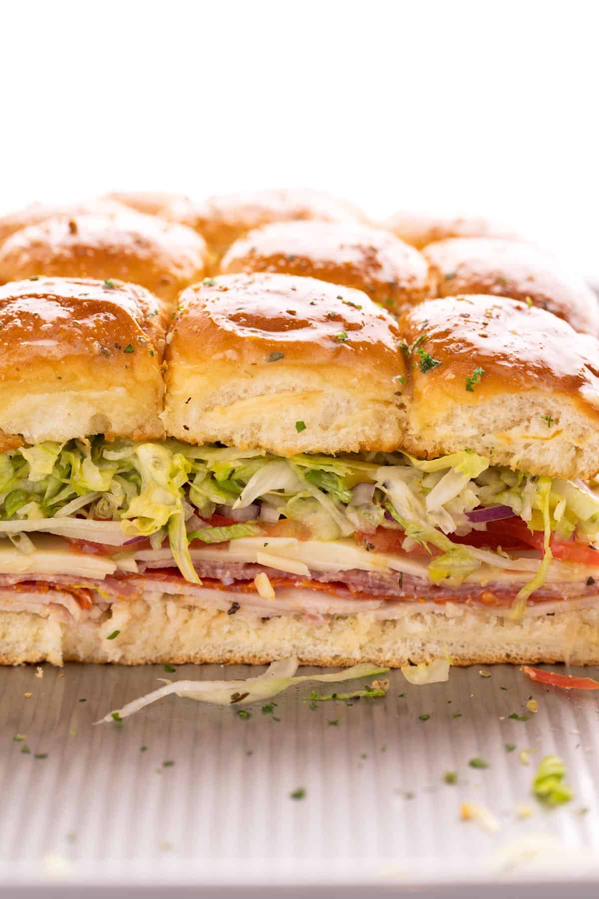 A tray of italian sliders topped with herbs.