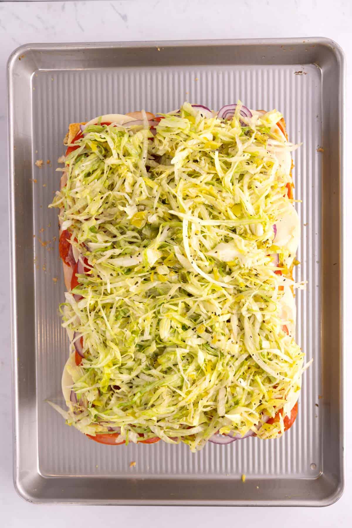 Thinly sliced lettuce added to sliders on a tray.