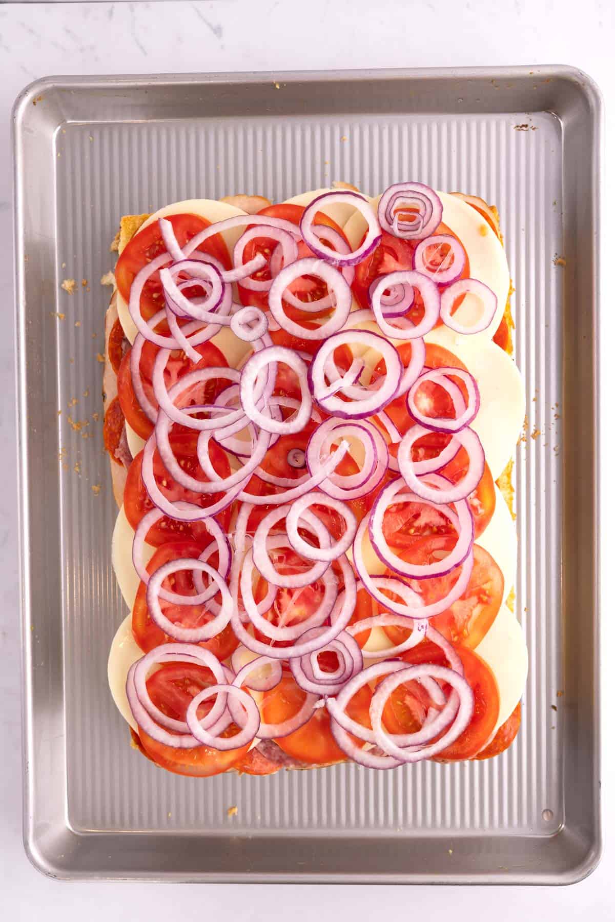 Onions spread onto half-assembled italian sliders.