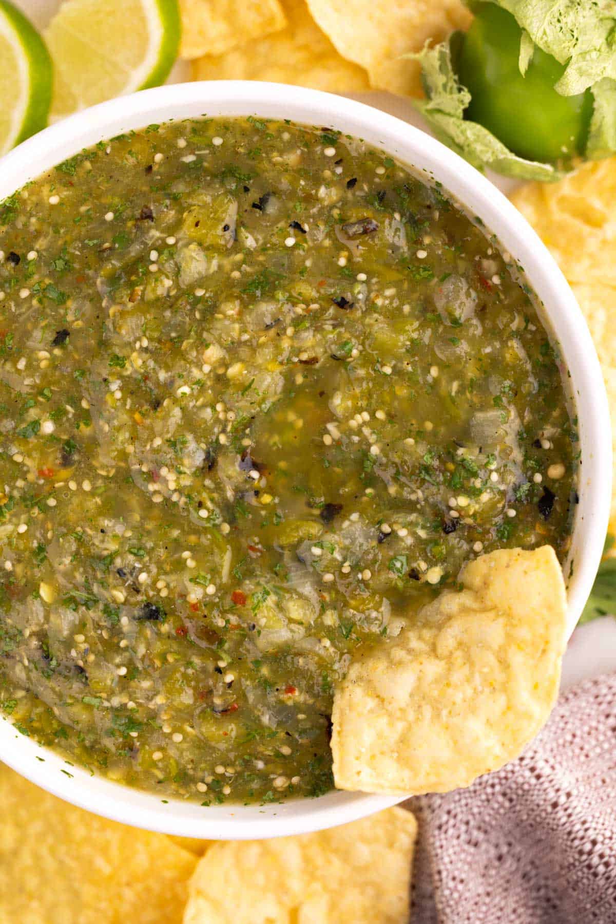 A bowl of tomatillo salsa surrounded by tortilla chips.