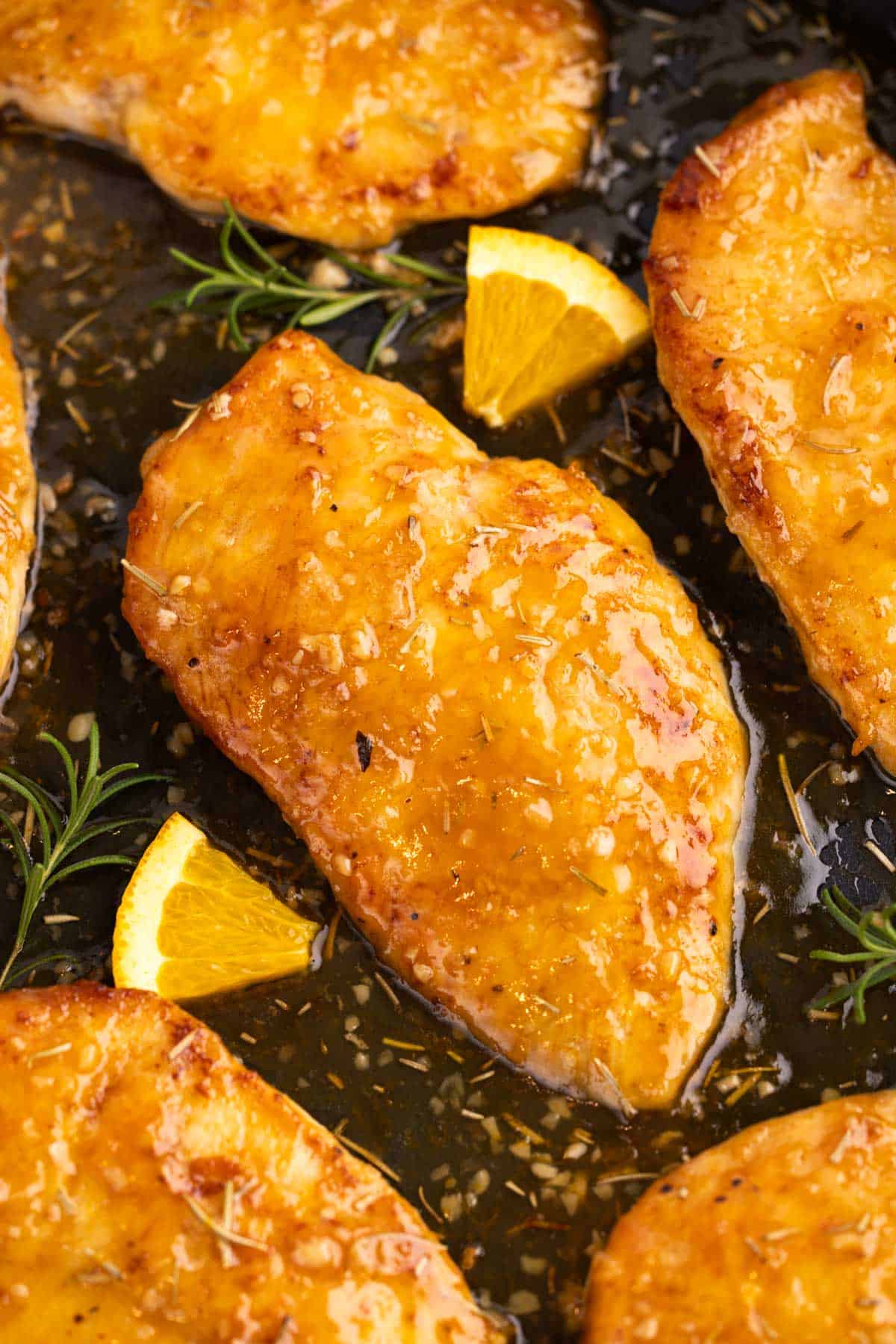 Chicken breasts with orange slices in a cooking pan.