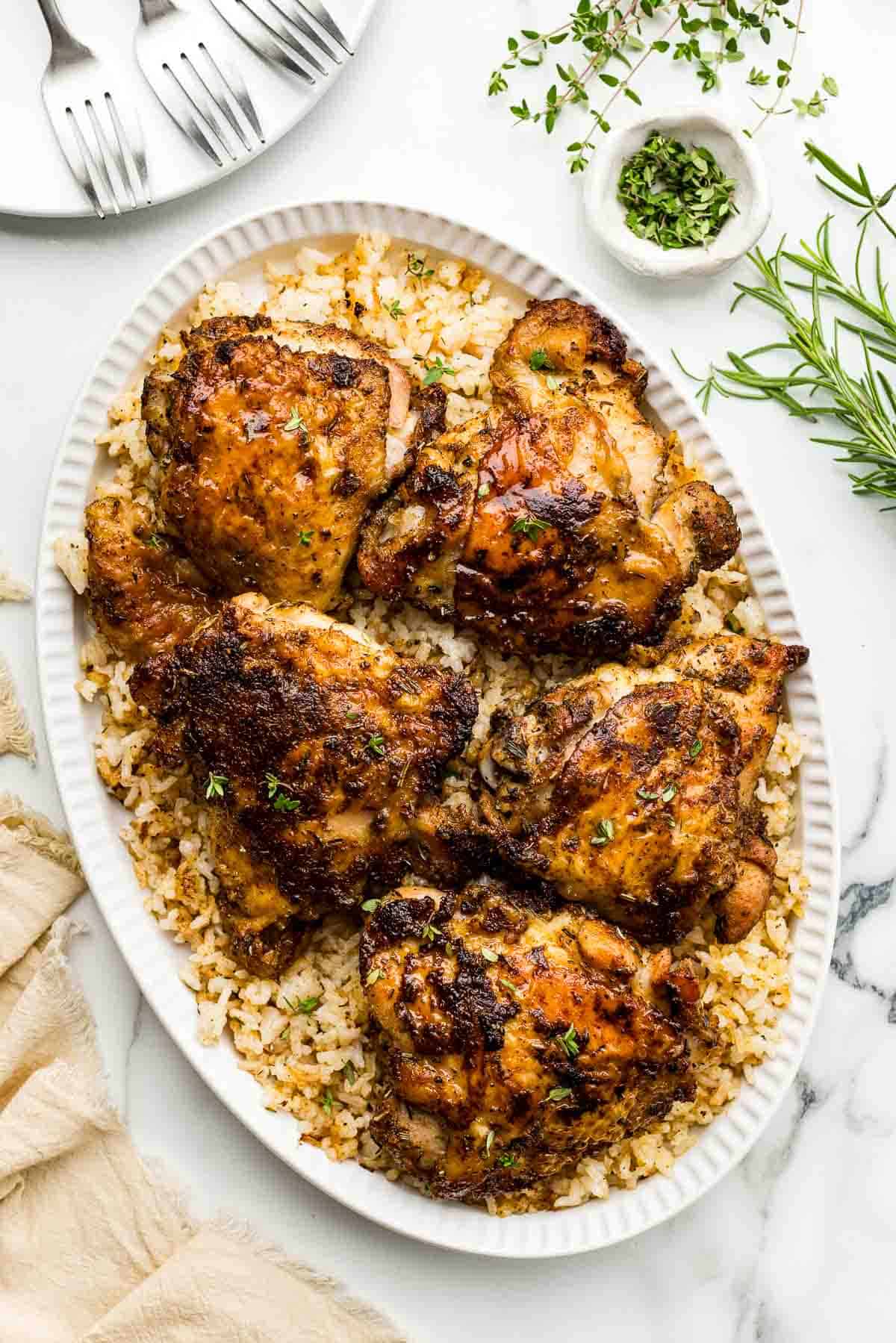 A small dish of herbs beside a large platter of chicken thighs on crispy rice.