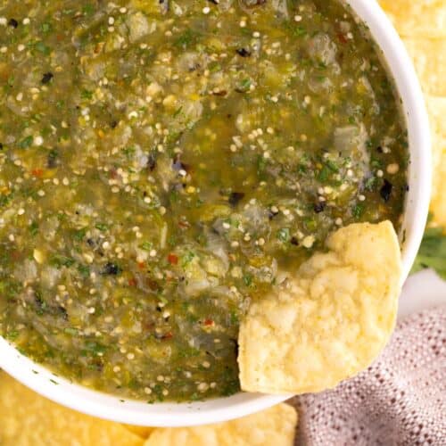Tomatillo salsa in a white bowl with a chip dipped in it.