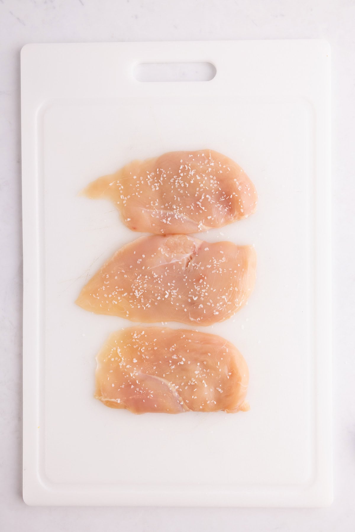 Seasoned raw chicken breasts on a plastic cutting board.