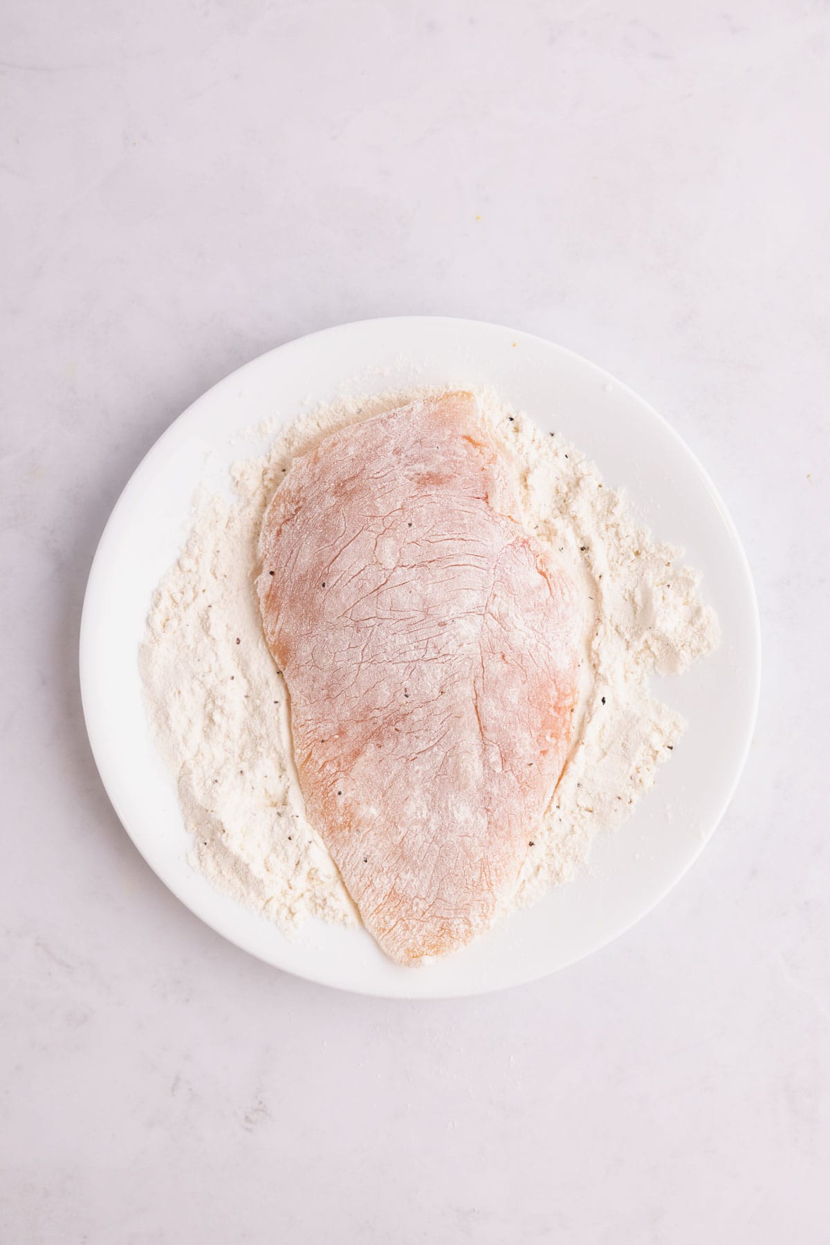 A chicken breast covered in flour on a plate.