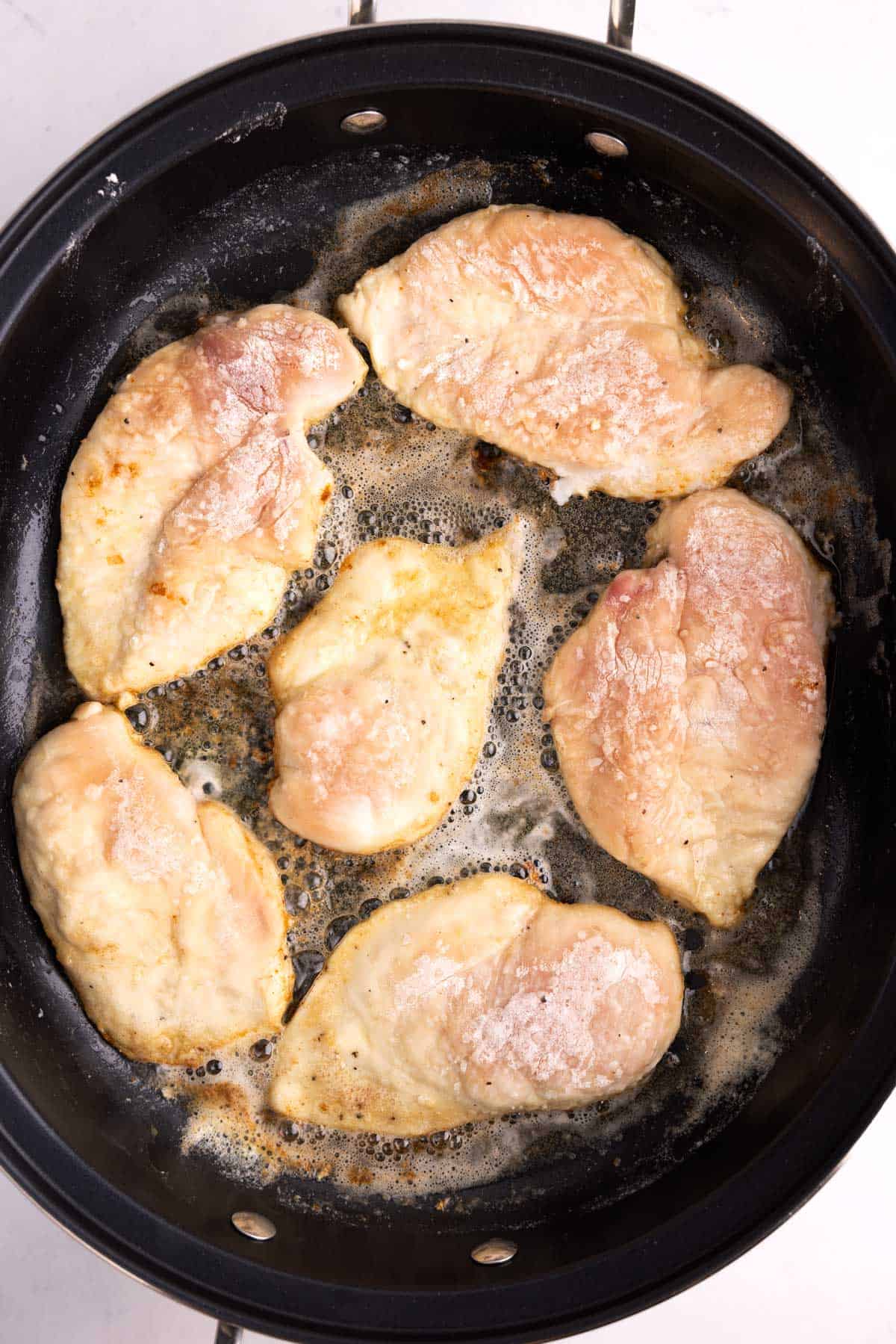 Raw chicken cooking in a large skillet.