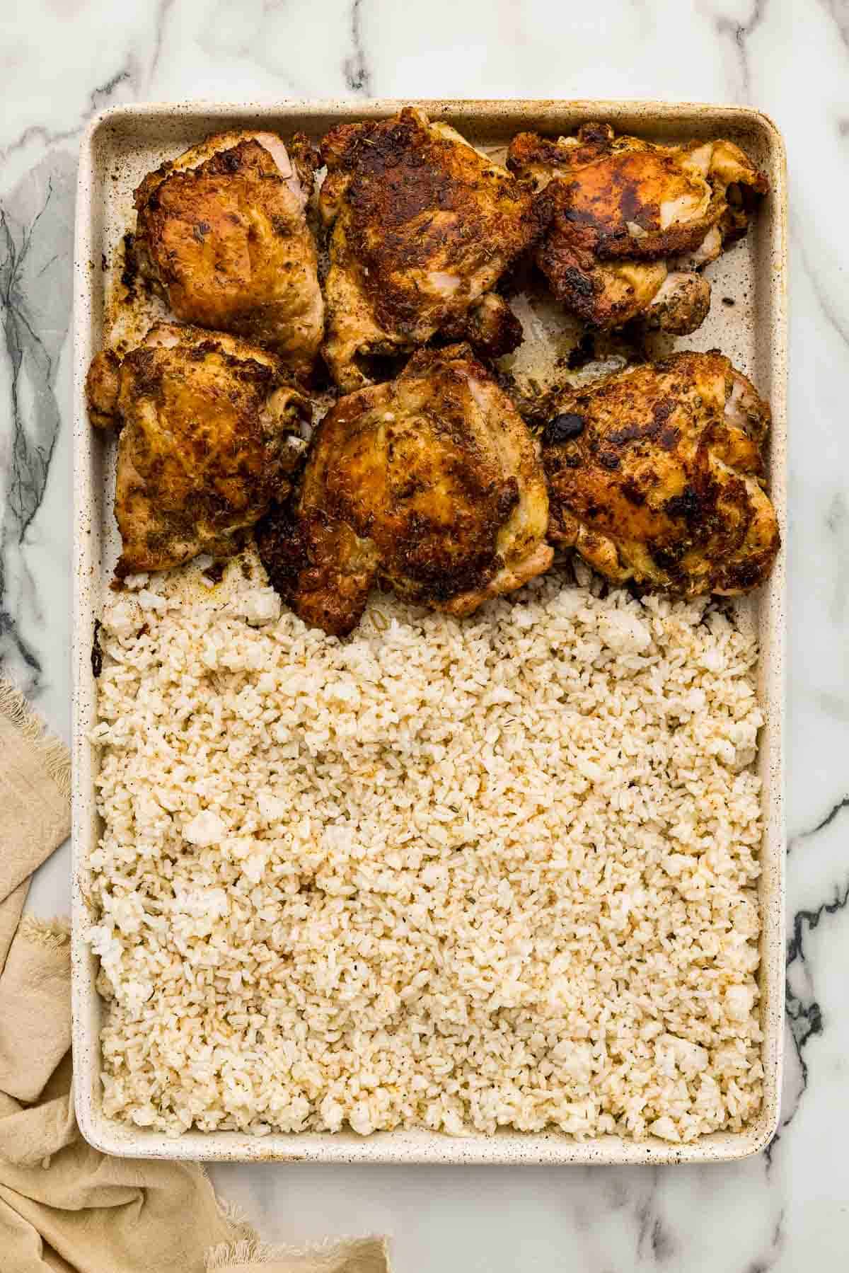 A sheet pan half full of chicken thighs and half full of rice.