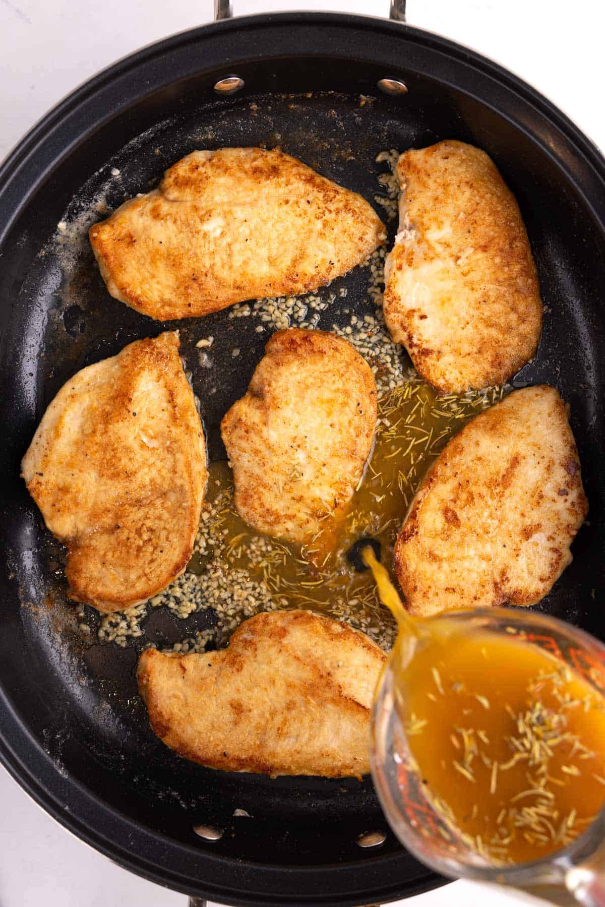 Maple orange glaze being poured into a pan of chicken breasts.