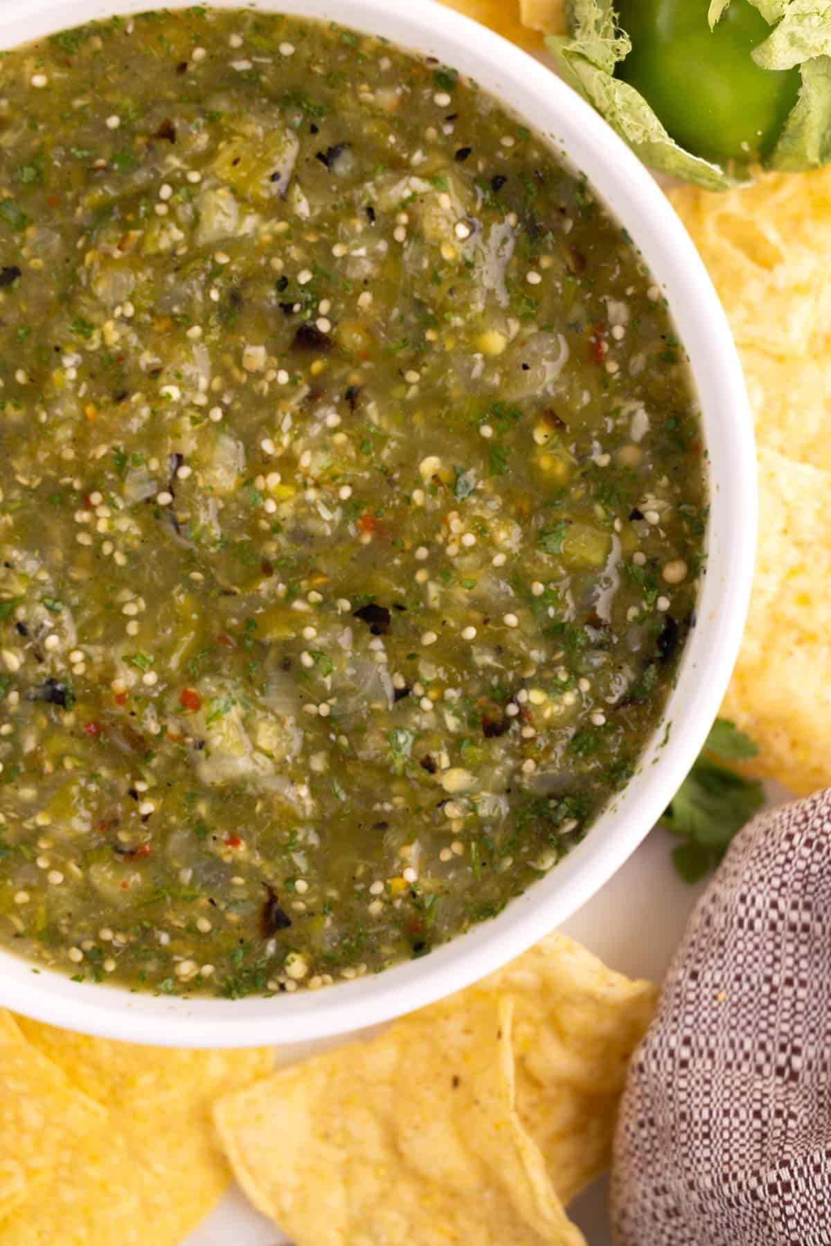 A serving dish filled with tomatillo salsa with an array of chips.
