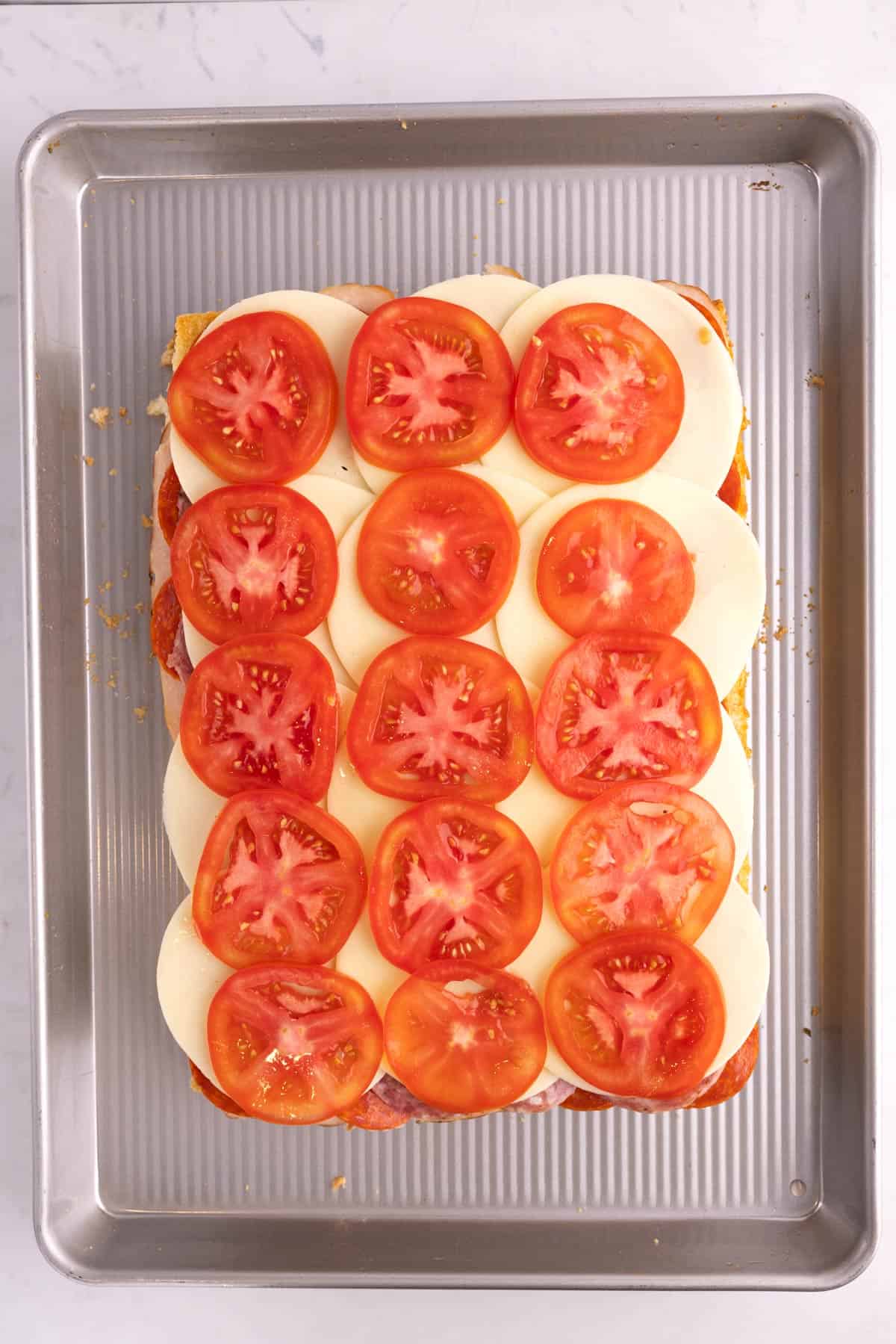 Tomatoes added to italian sliders on a sheet pan.
