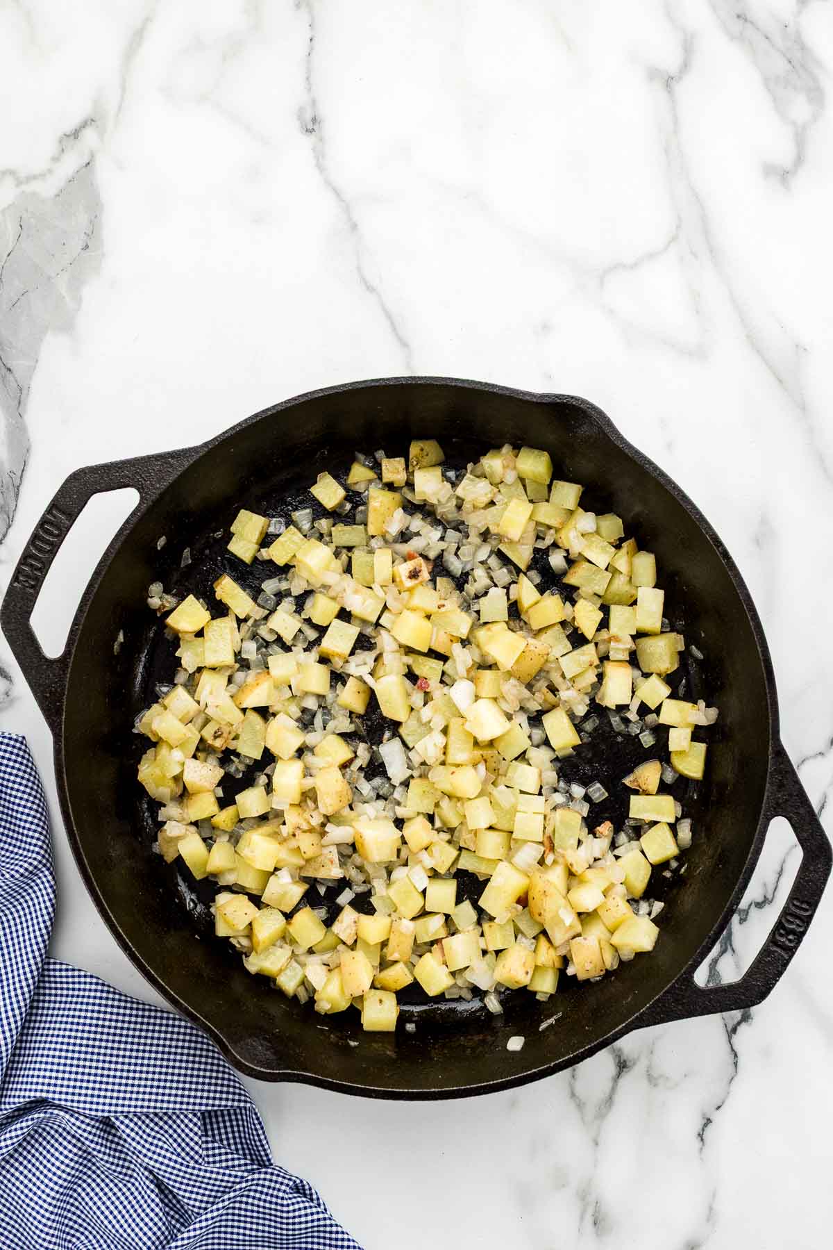 Potatoes and onions in mixed in a cooking skillet.