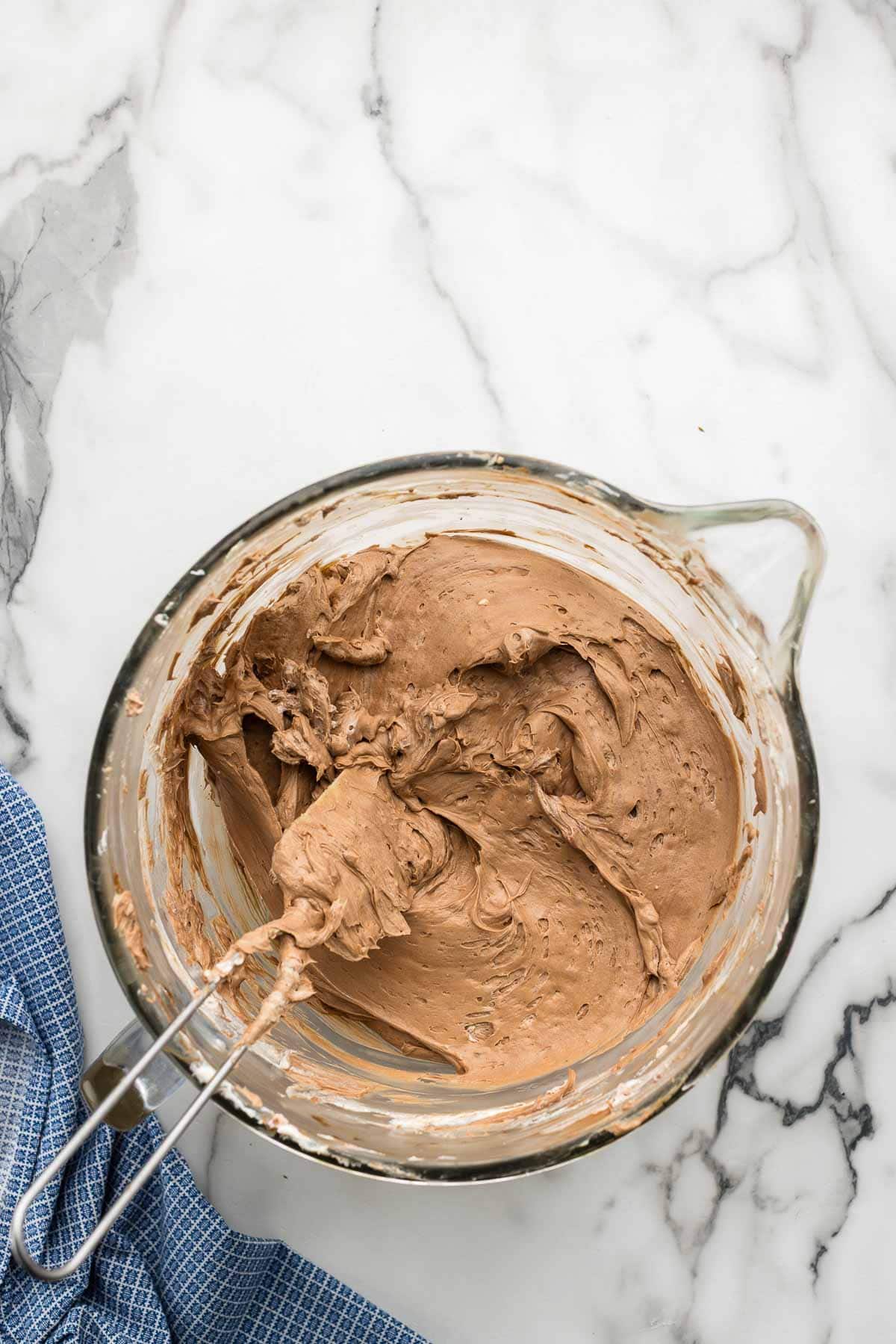 A spatula dipped in a bowl of chocolate cheesecake batter.