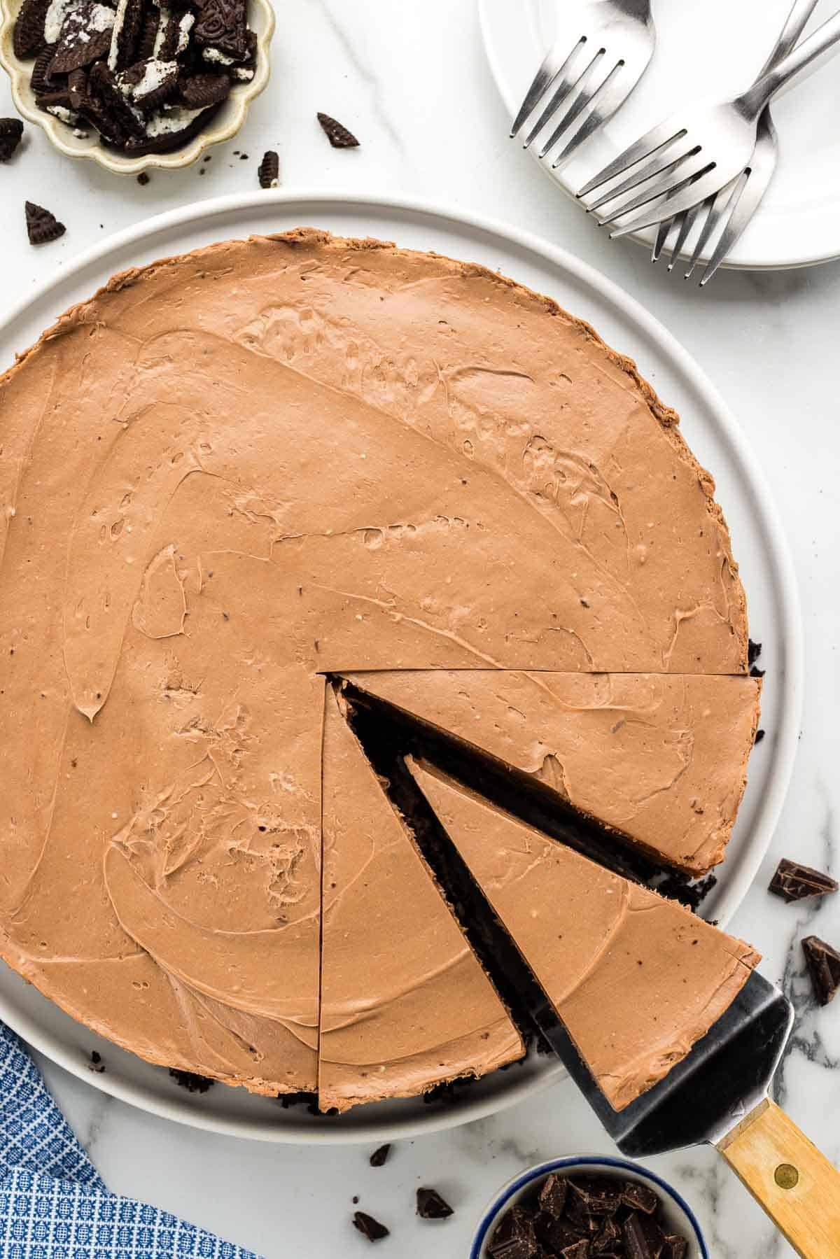 Sliced chocolate cheesecake with a single piece being pulled out with a serving tool.