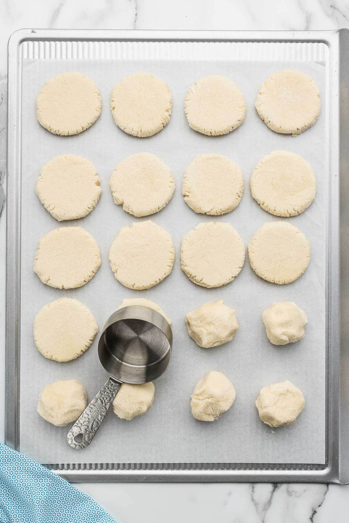 A measuring cup pressing dough balls flat on a cookie sheet.
