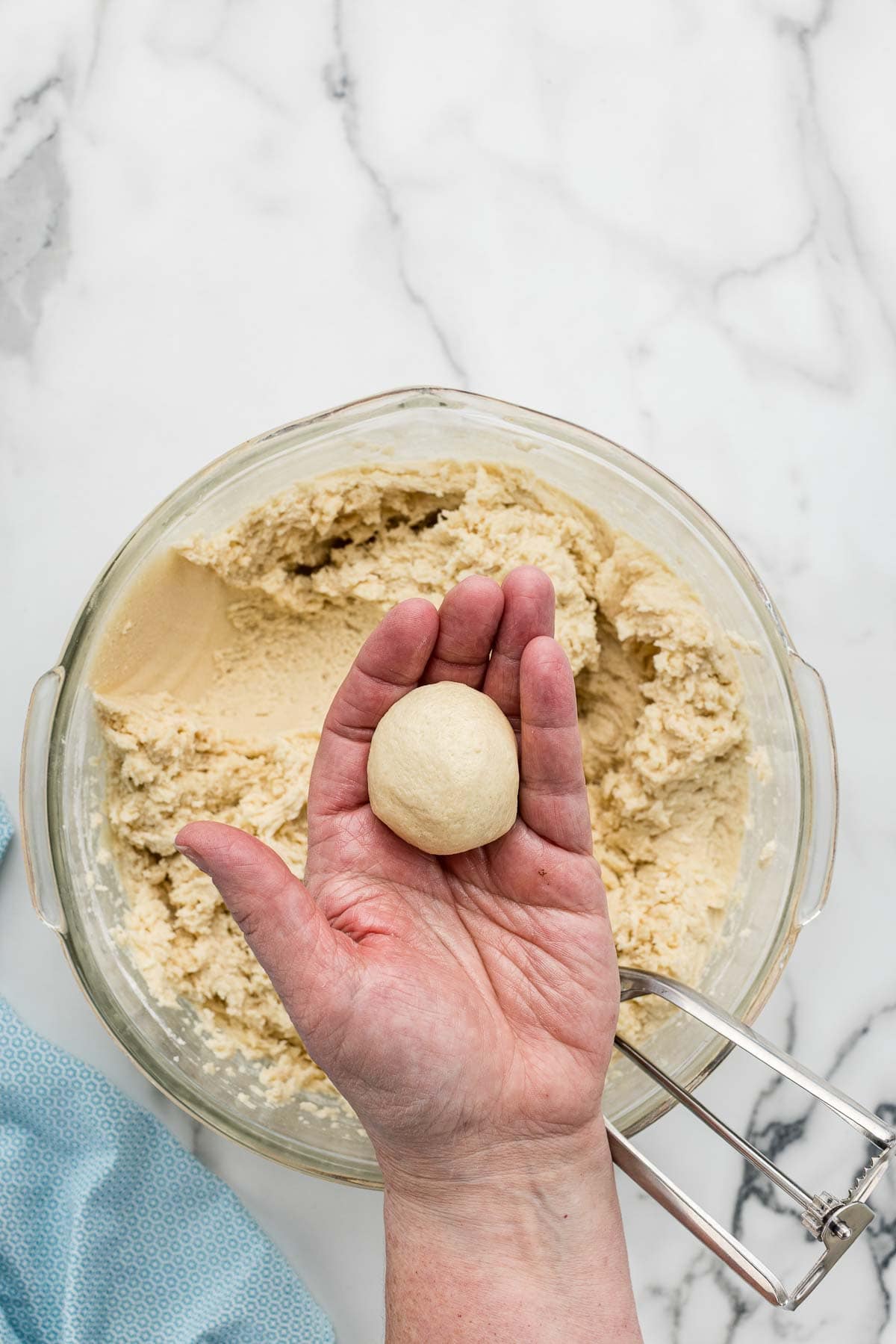 A dough ball being held over a bowl of cookie dough.