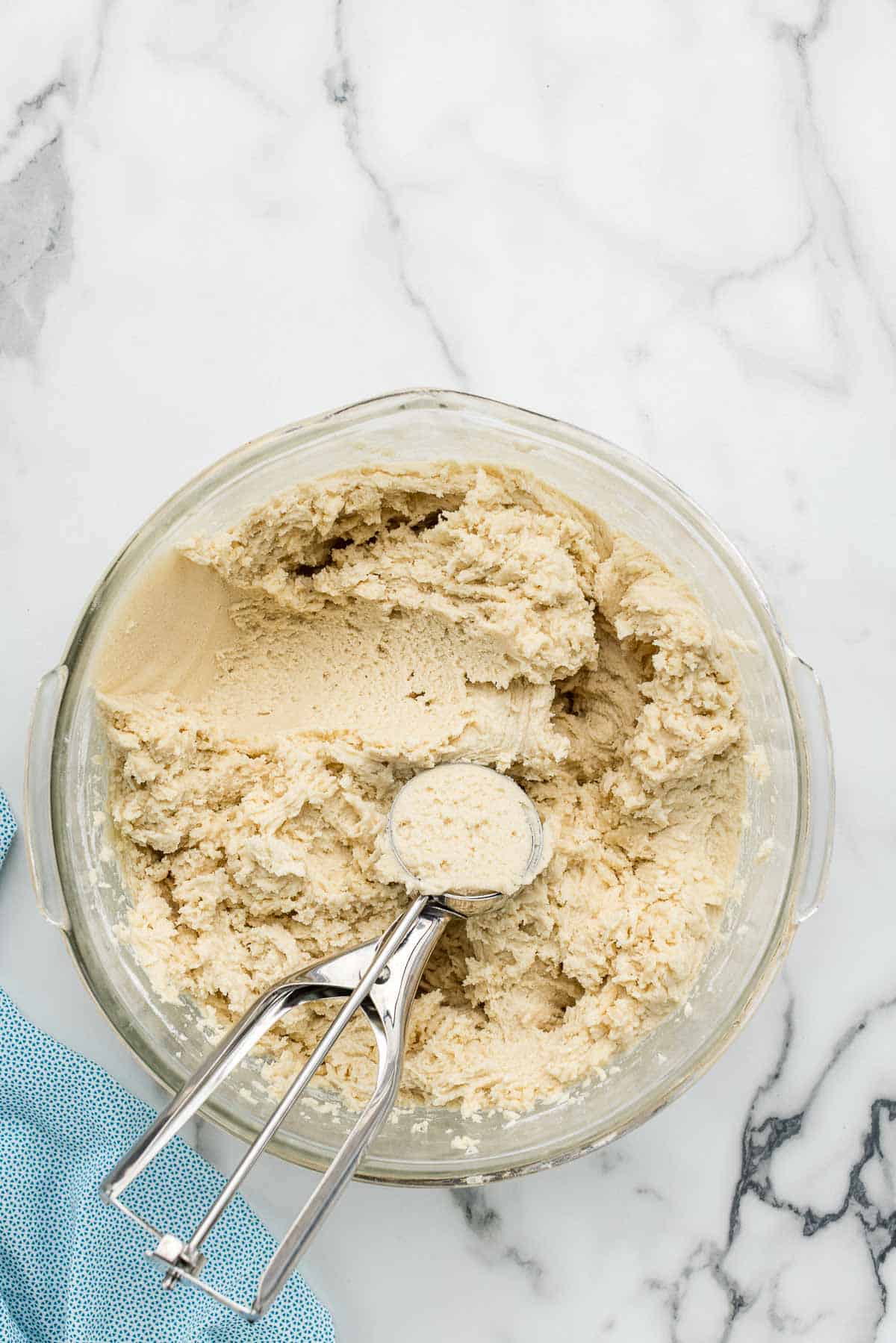 A dough scooper sitting in a glass bowl of cookie dough.