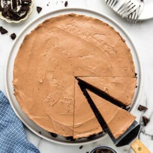 A chocolate cheesecake with a slice being taken out on a serving platter.