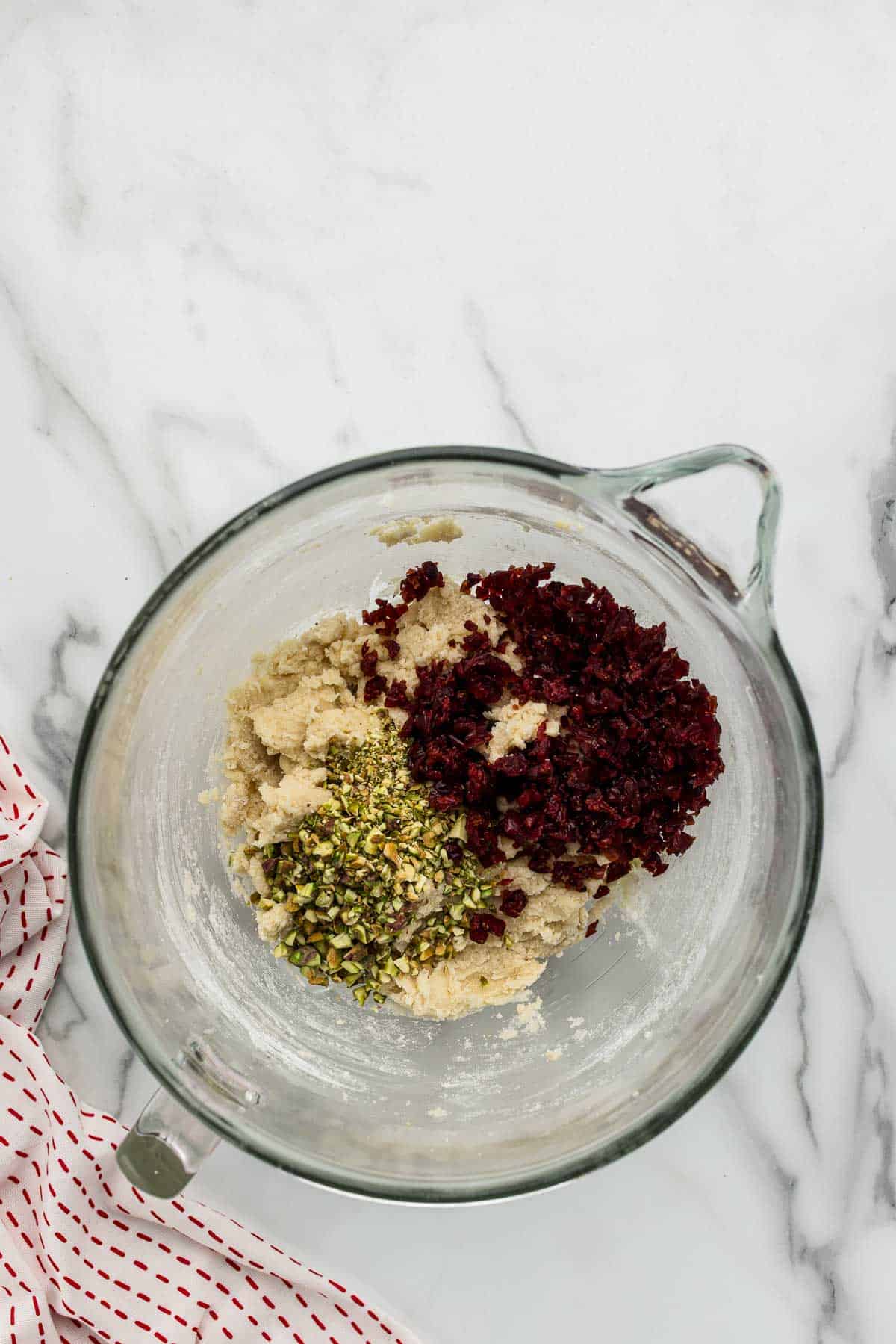 Cranberried and pistachios added to cookie dough in a large glass measuring bowl.