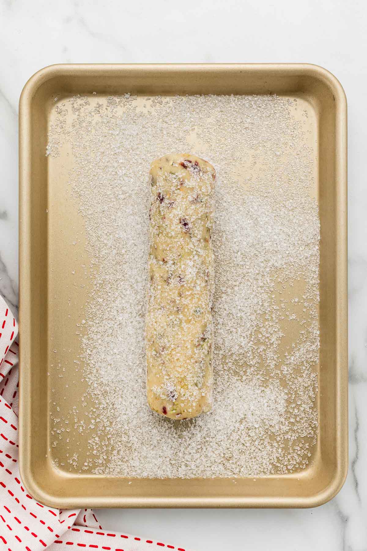 A cookie dough log on a sheet pan covered in sugar.