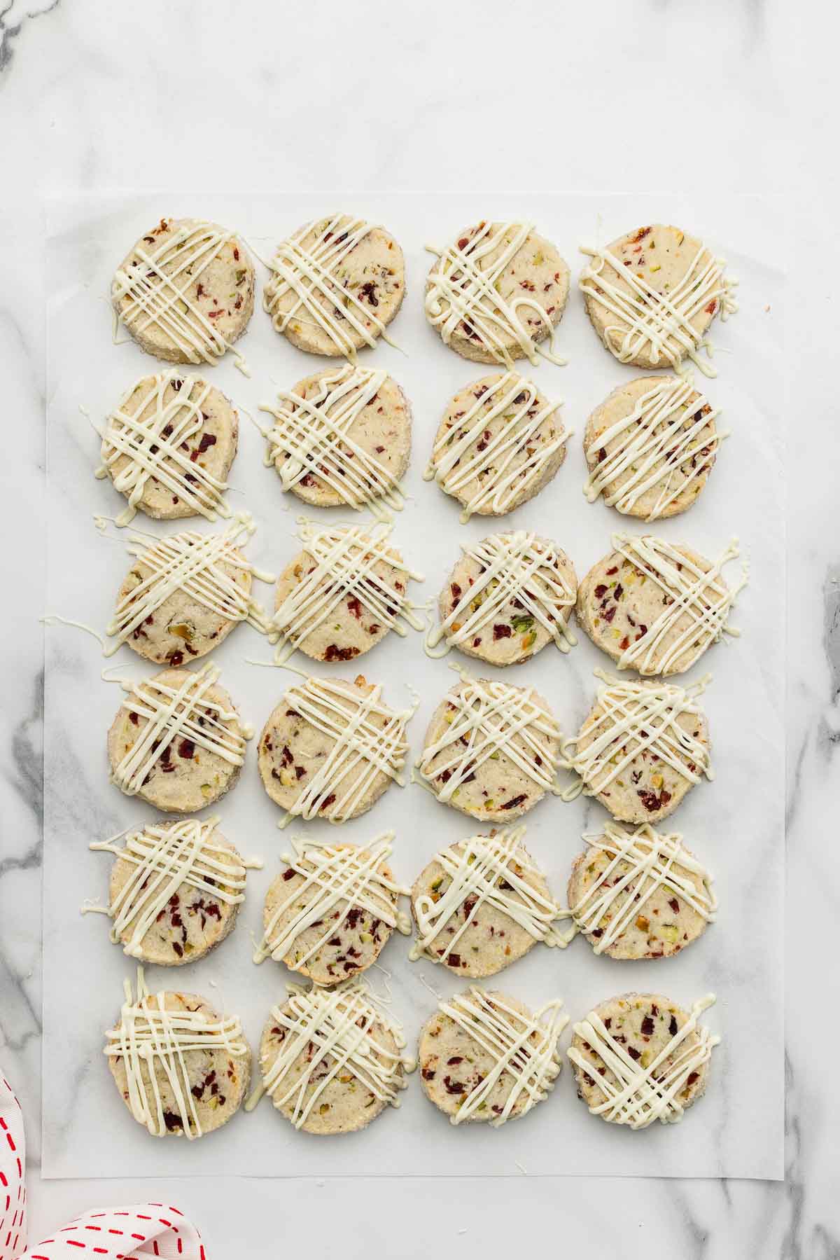 Baked shortbread cookies on parchment drizzled with white chocolate.