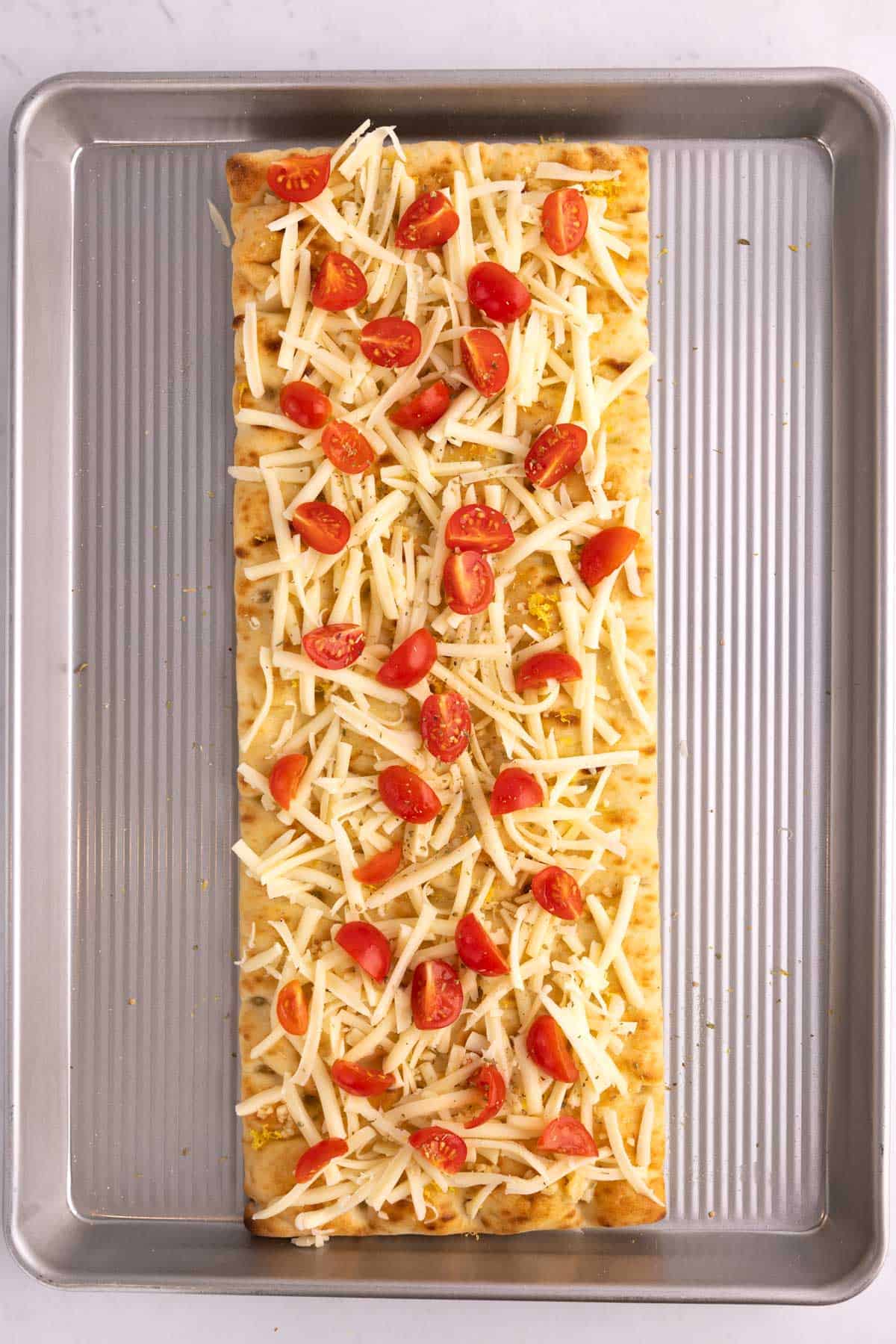 Flatbread piled with cheese and tomatoes on a pan.