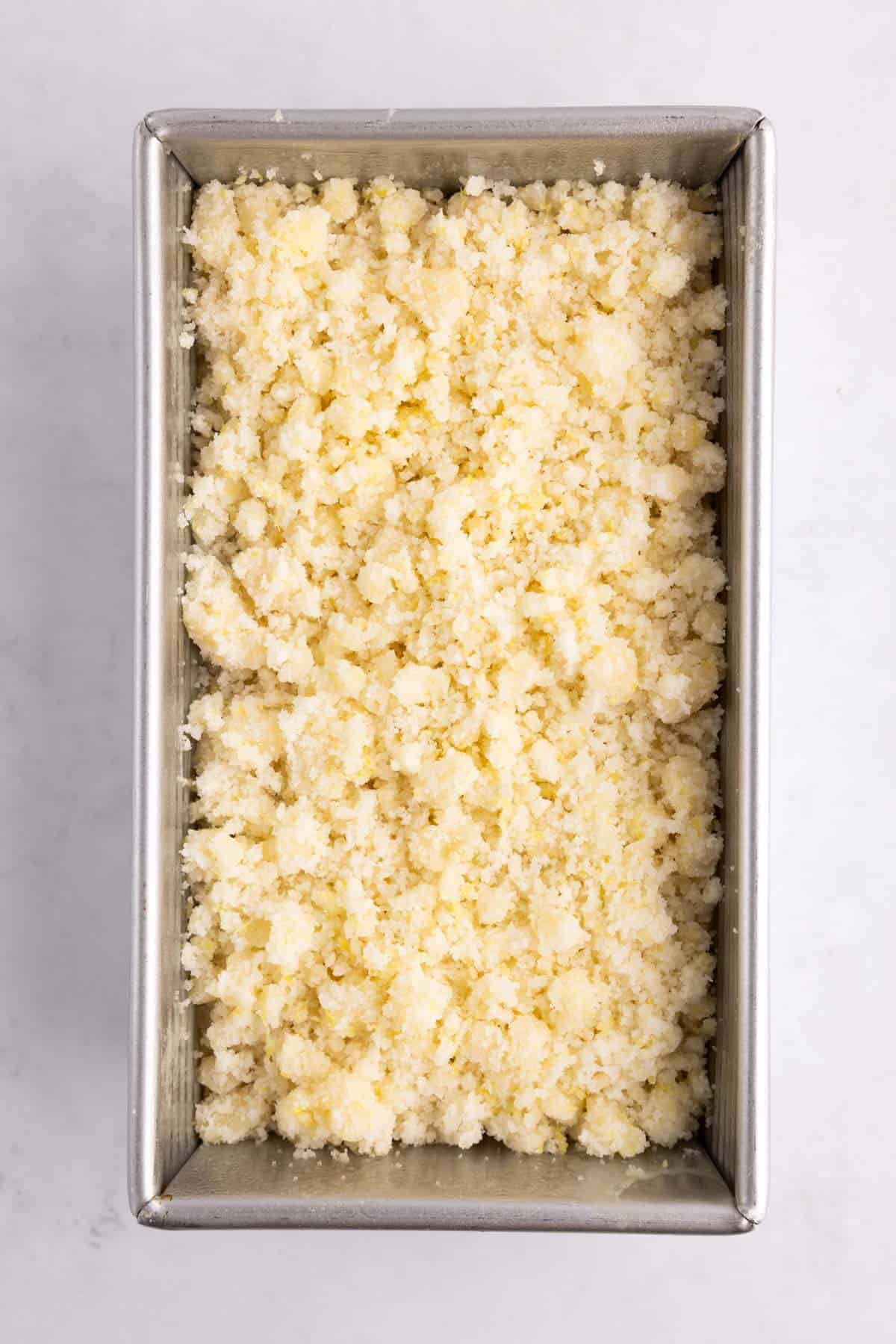 Streusel added on top of bread dough in a loaf pan.