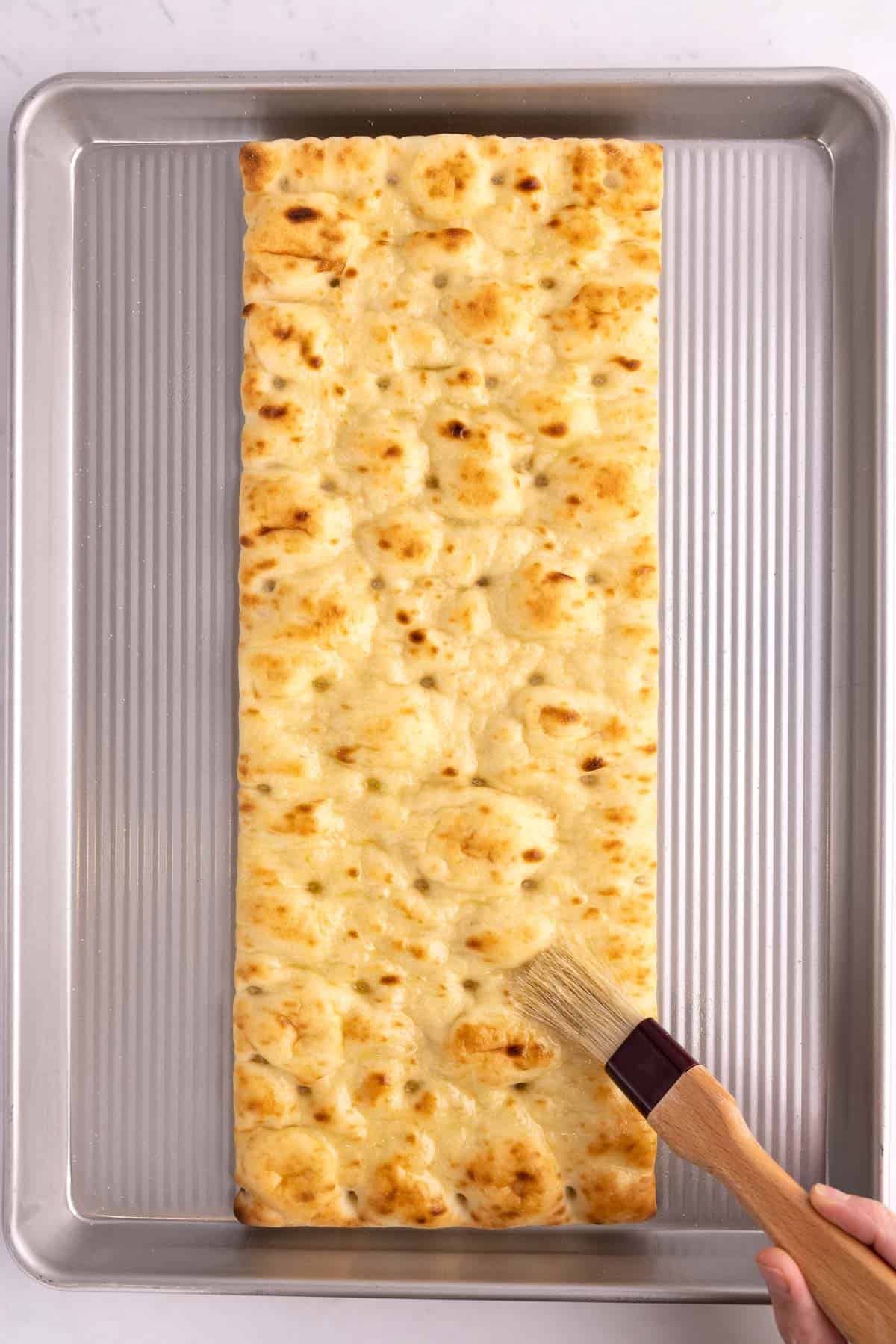 Flatbread on a pan getting brushed with oil.