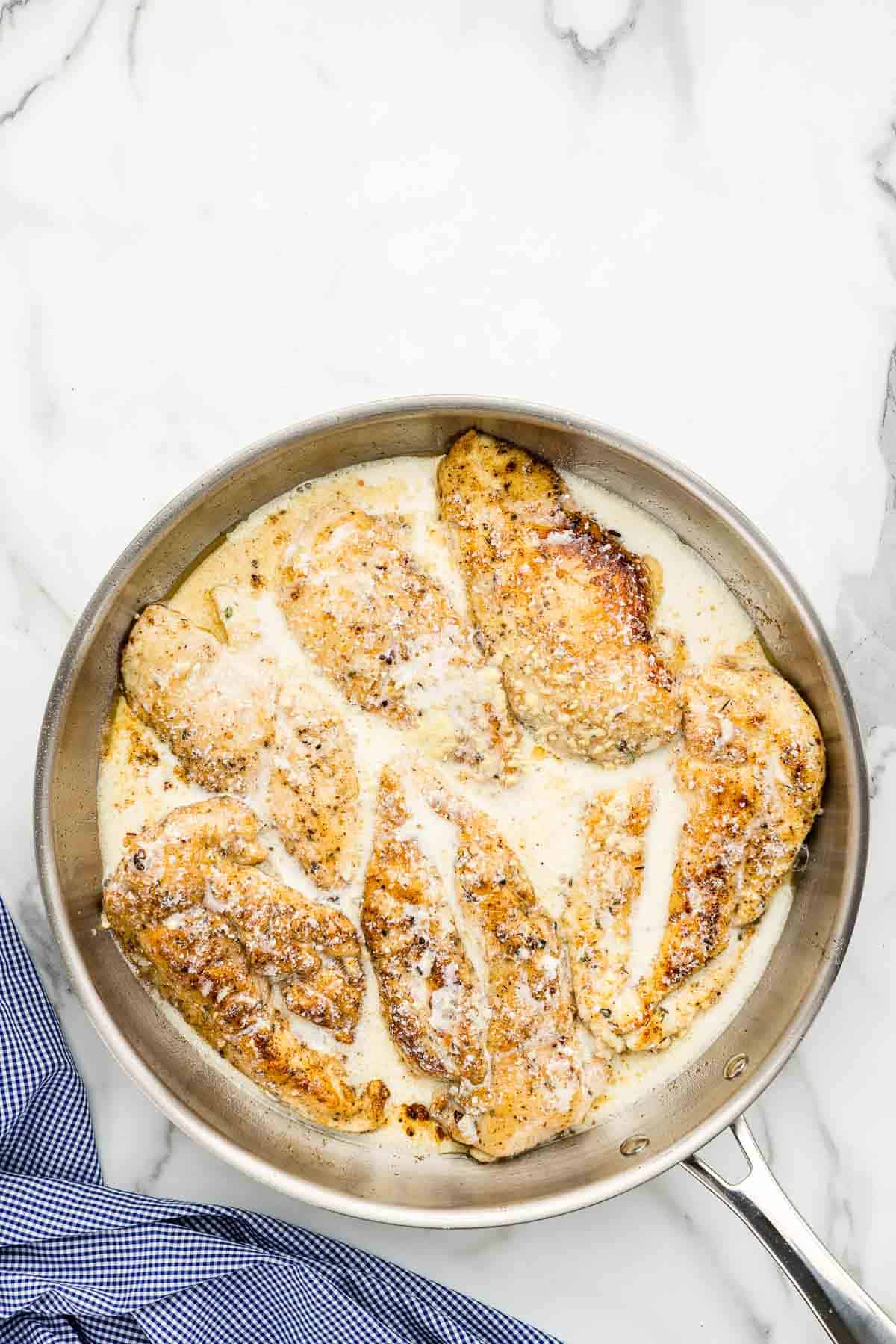 A large pan of cooked chicken breasts with creamy sauce.