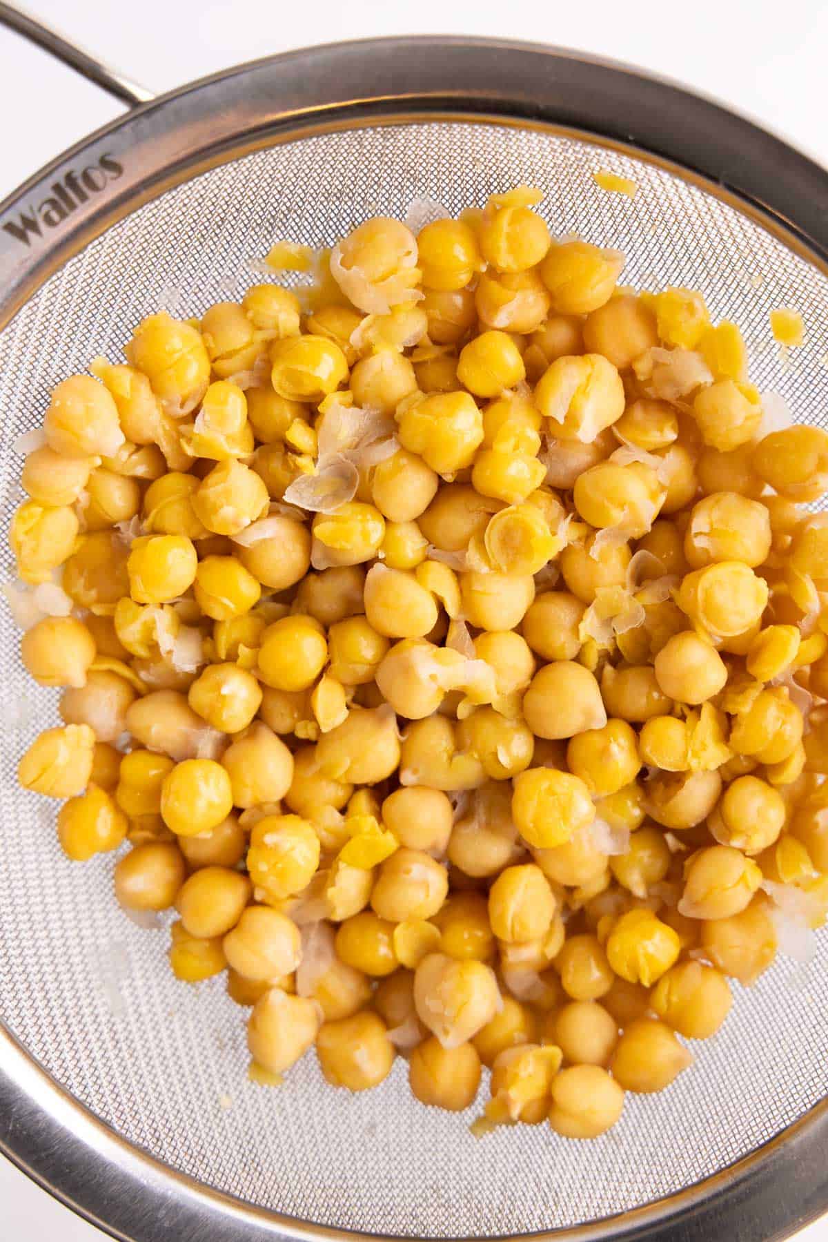 Chickpeas sitting in a wire mesh strainer.