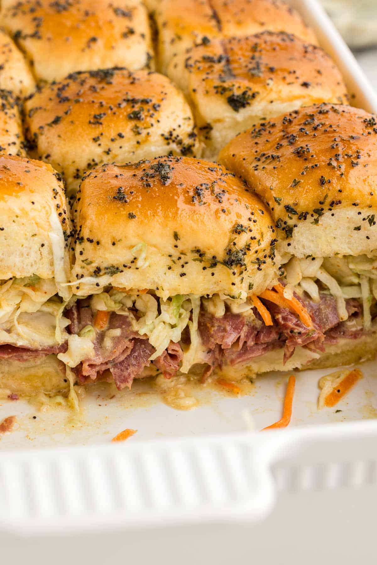 A glass baking pan full of pastrami sliders.