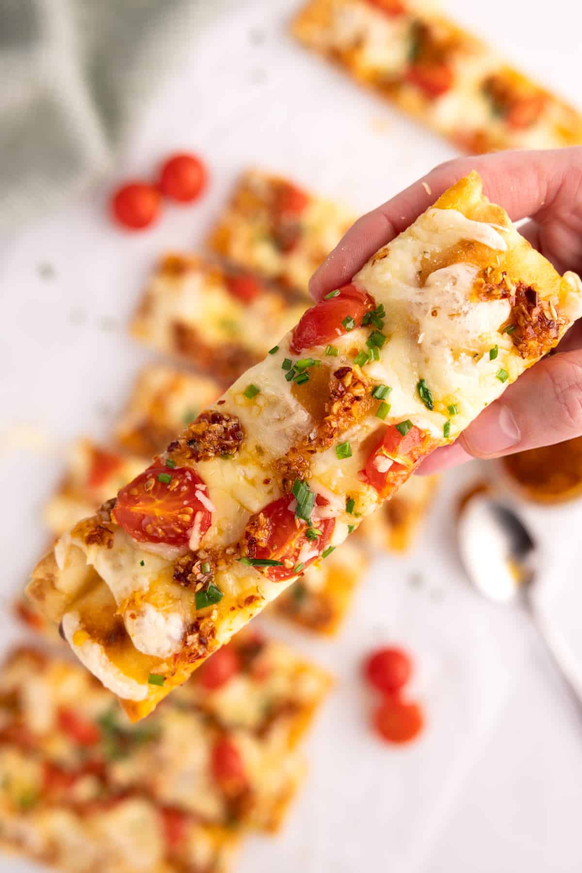 Holding a slice of flatbread pizza over a row of more pizza slices.