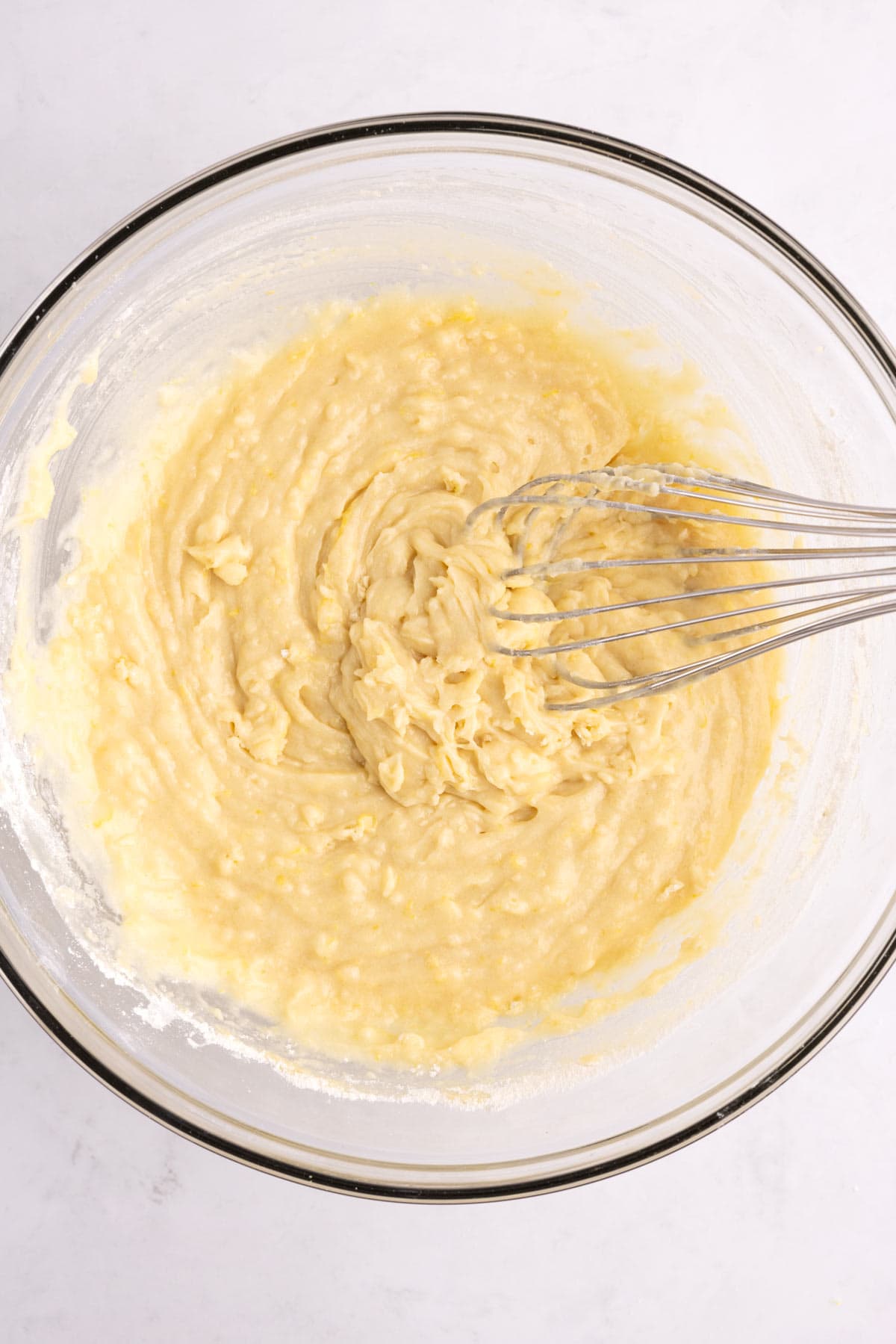 A whisk mixing lemon blueberry ingredients together in a large glass dish.