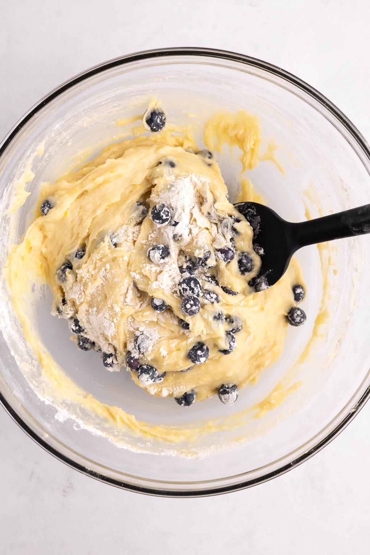 A rubber spatula combining blueberries into a bowl full of bread dough.