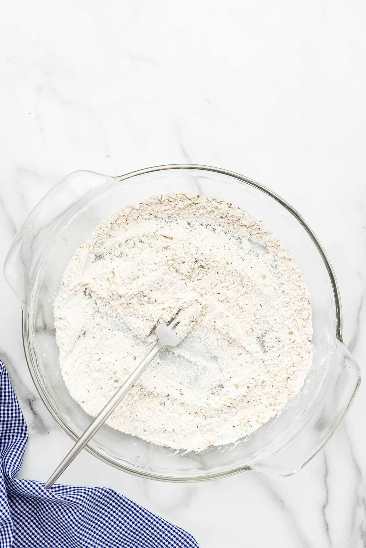 A shallow dish full of a flour mixture with a fork in it.