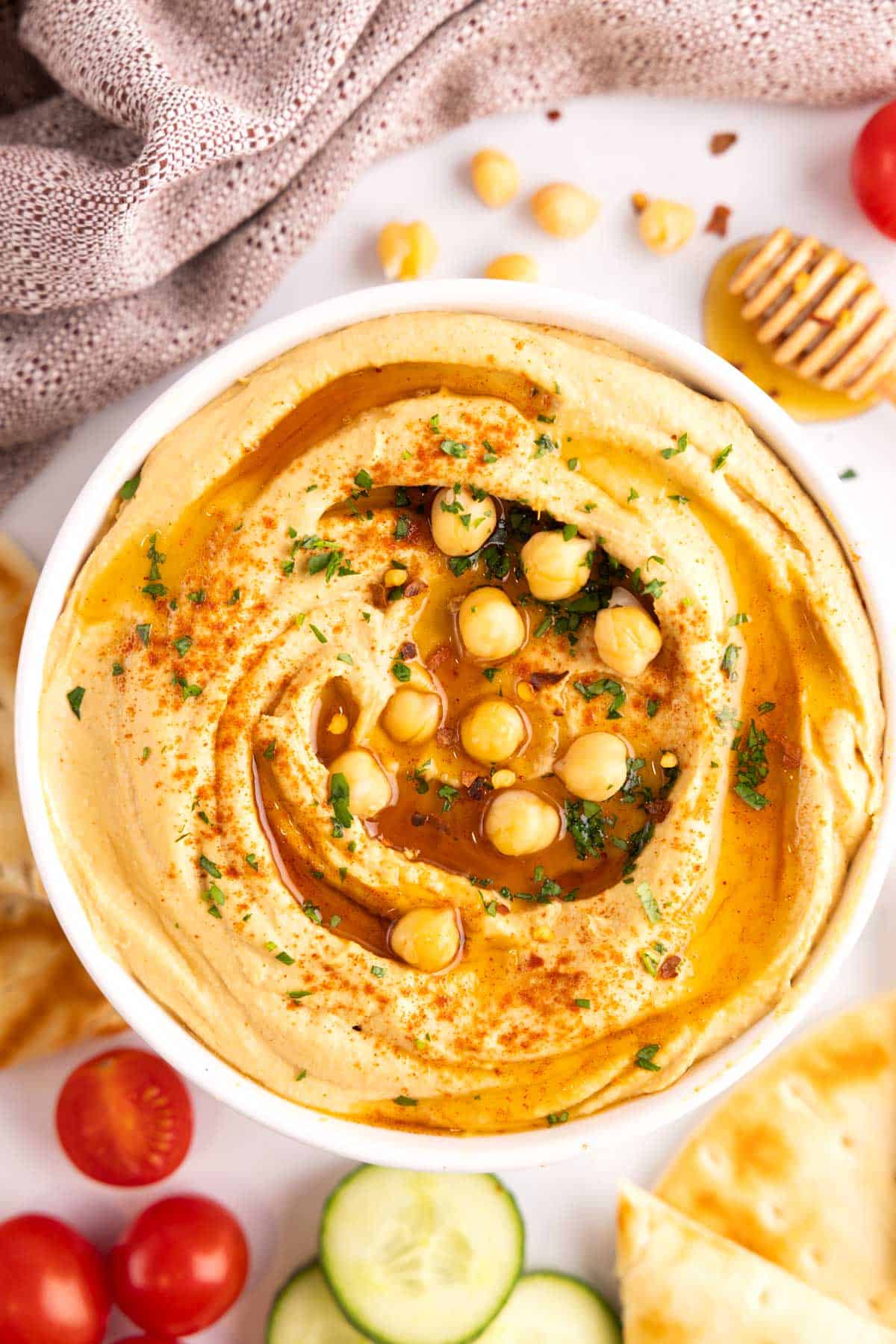 A bowl of hot honey hummus surrounded by an array of veggies and bread to dip into it.