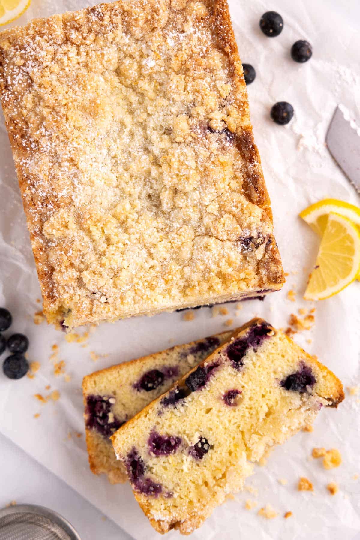 Half of a loaf of lemon blueberry bread with slices piled beside it.
