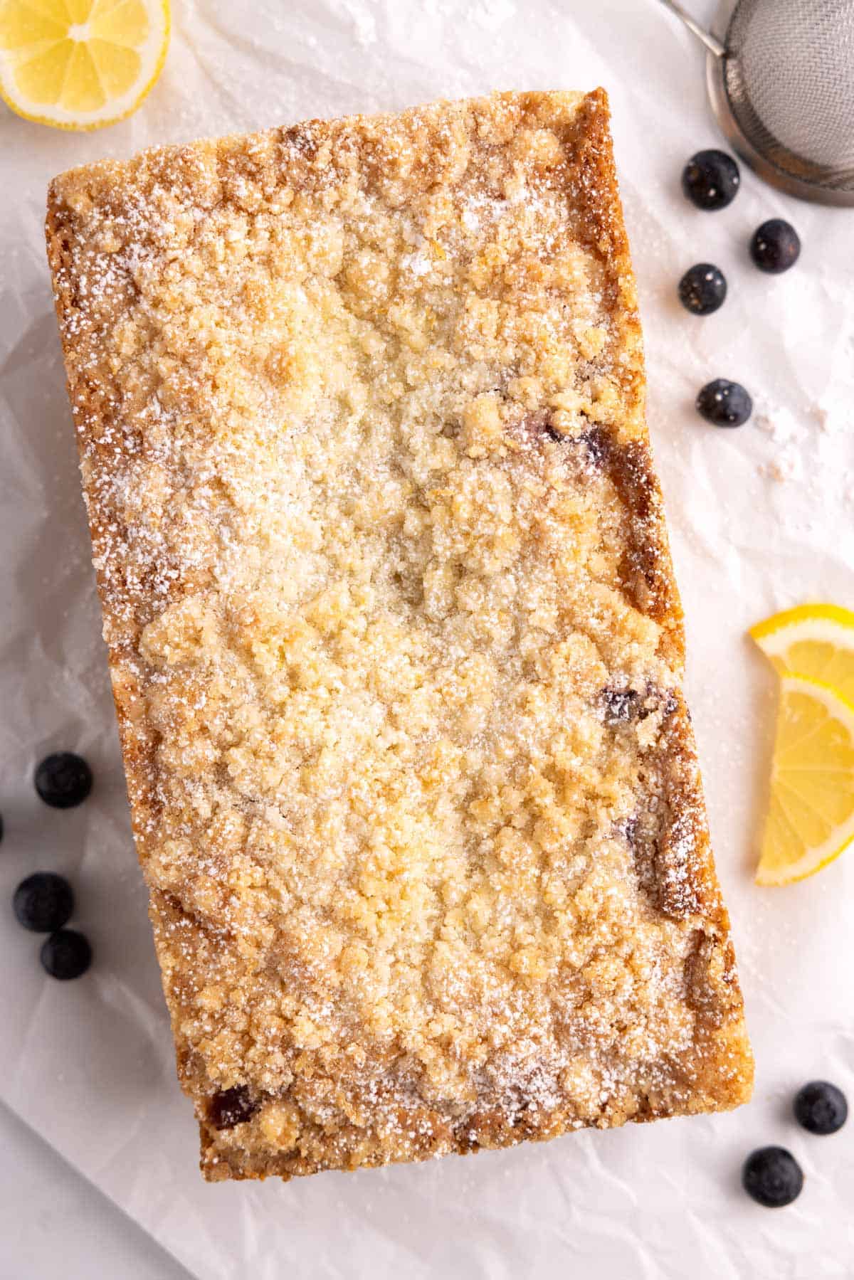 Lemon blueberry bread on parchment with fresh blueberries beside it.
