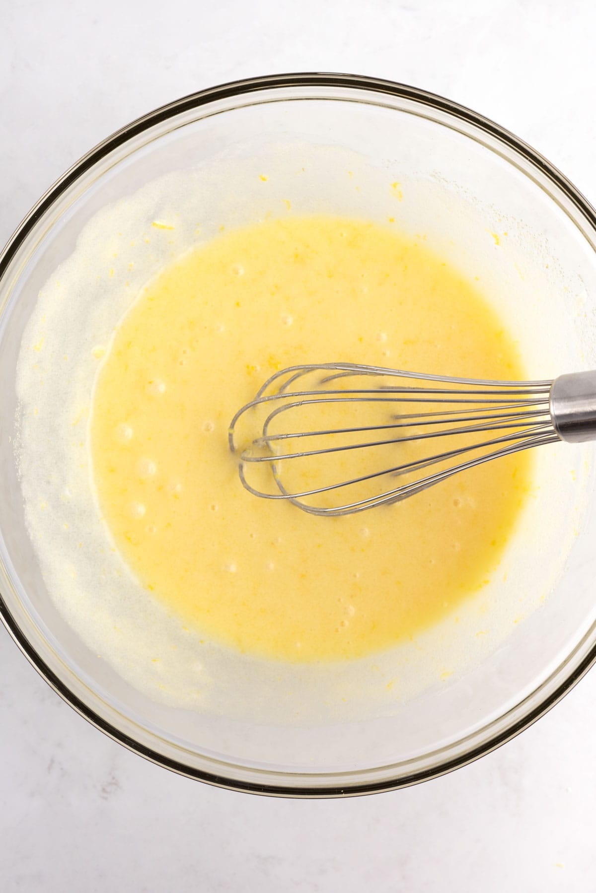 Blueberry bread ingredients being mixed in a glass bowl with a whisk.