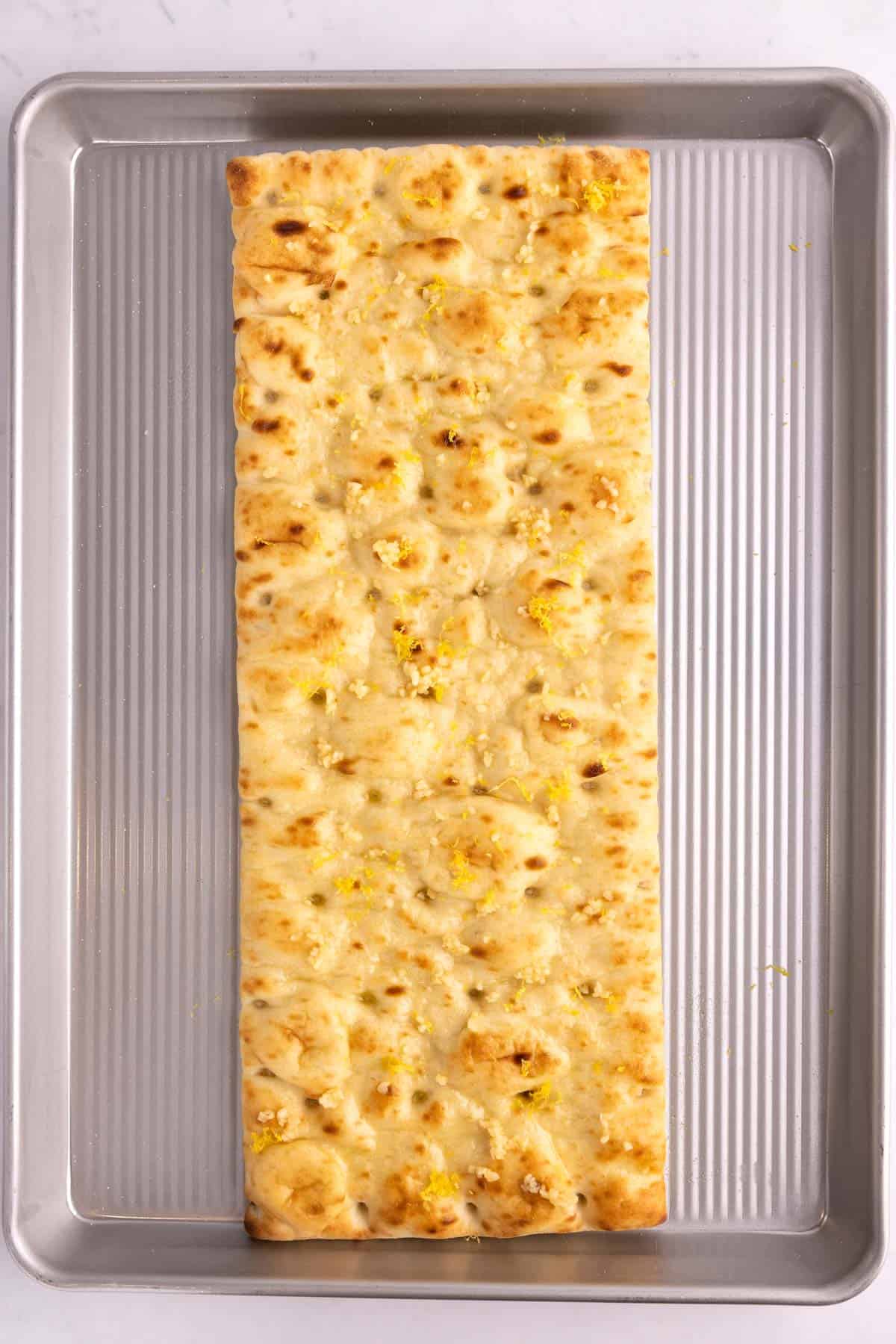 Pizza crust on a pan sprinkled with lemon zest.