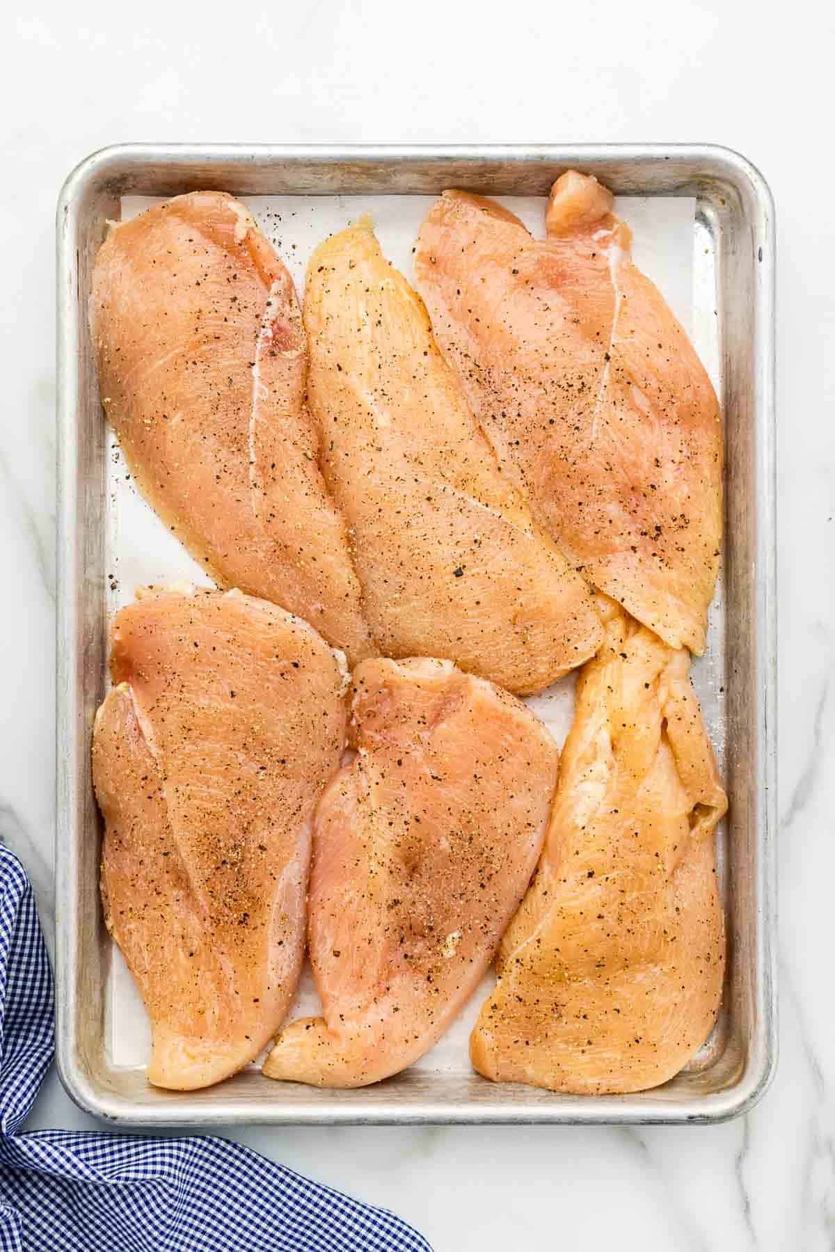 Raw, seasoned chicken breasts on a large sheet pan.