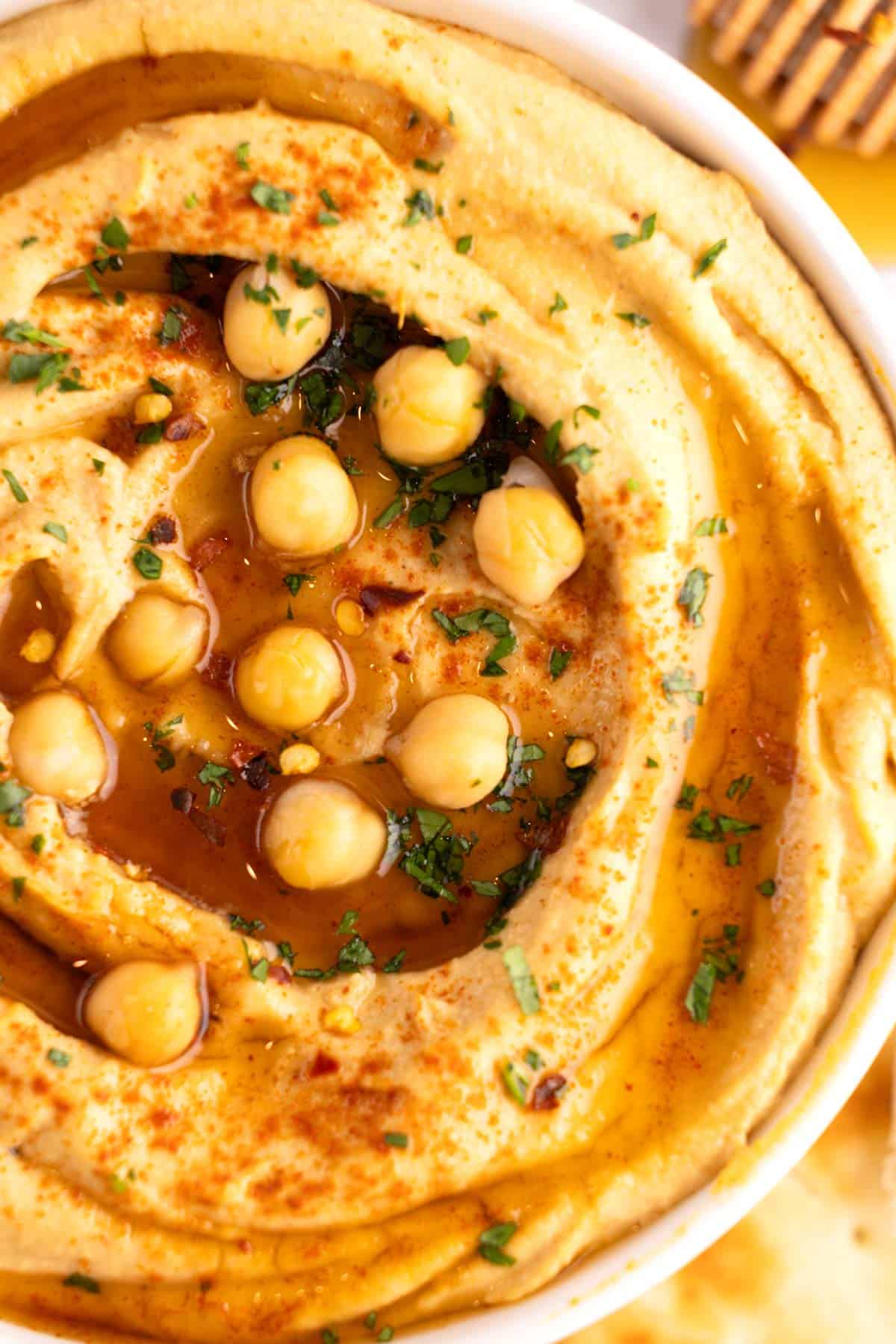 Closeup of hummus drizzled with hot honey in a white glass bowl.