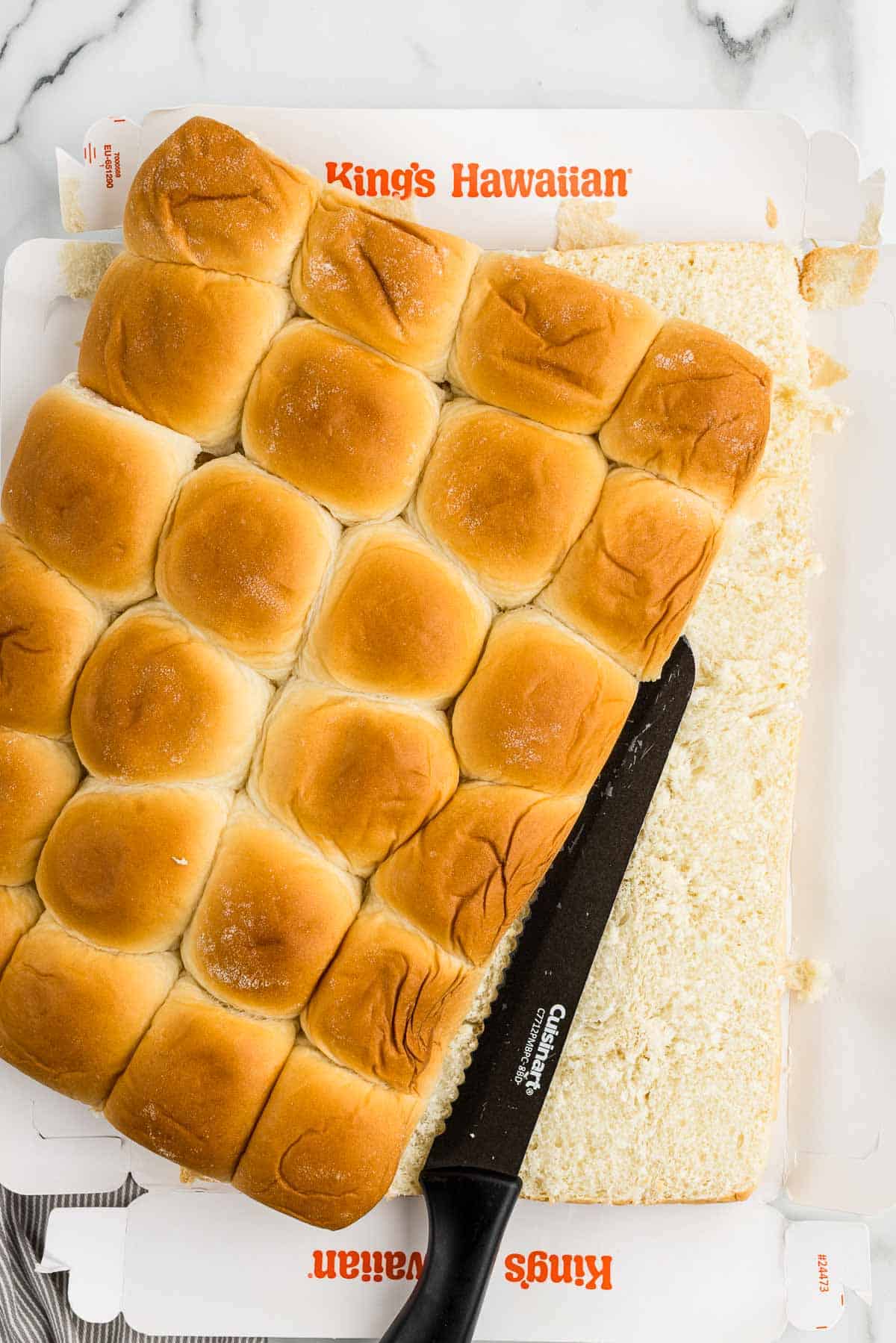 A bread knife resting in between two halves of cut Hawaiian rolls.
