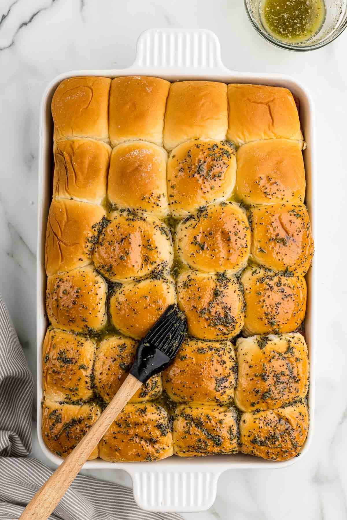Brushing sauce on assembled sliders with a silicone brush.