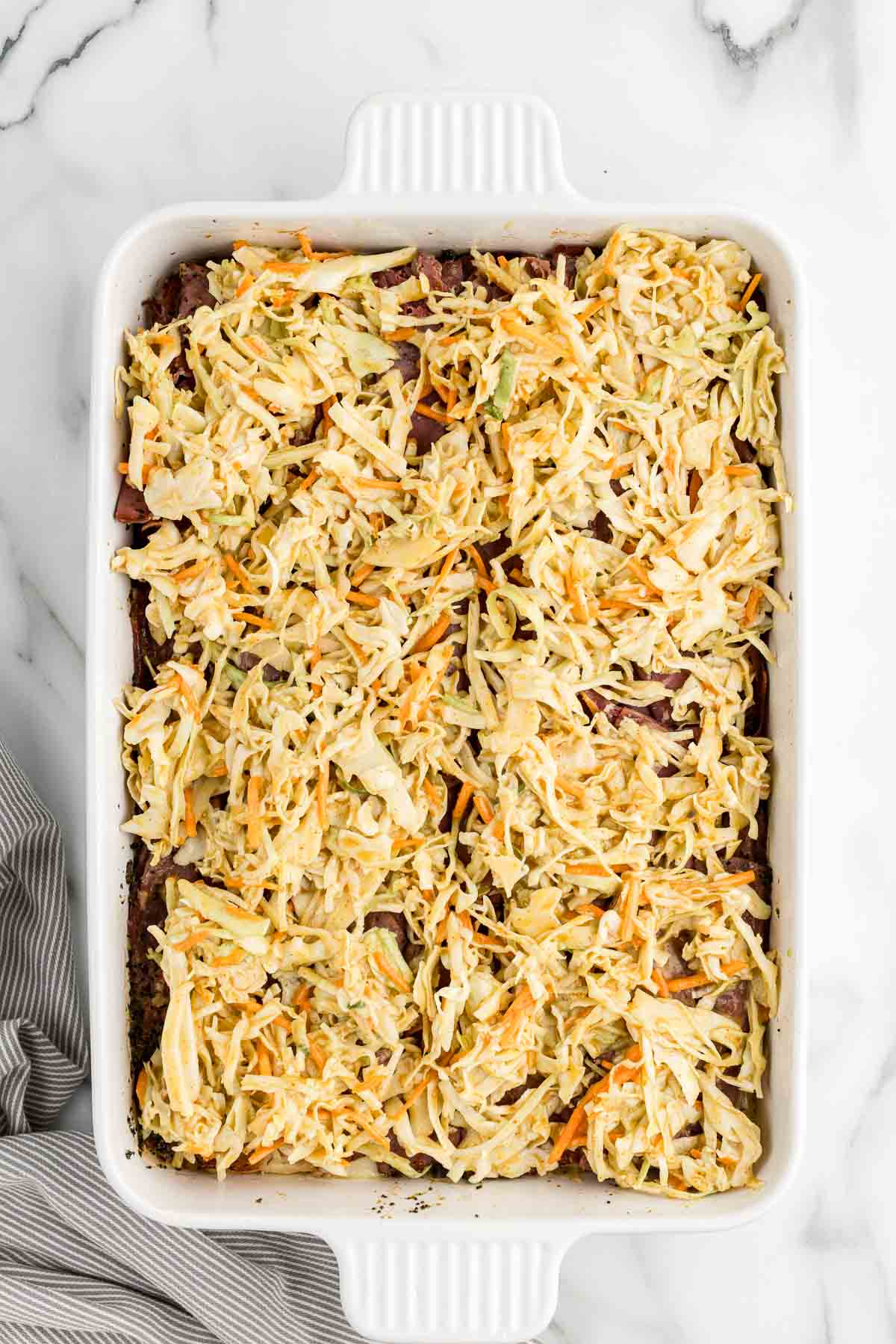 Coleslaw layered on top of meat in a baking dish.